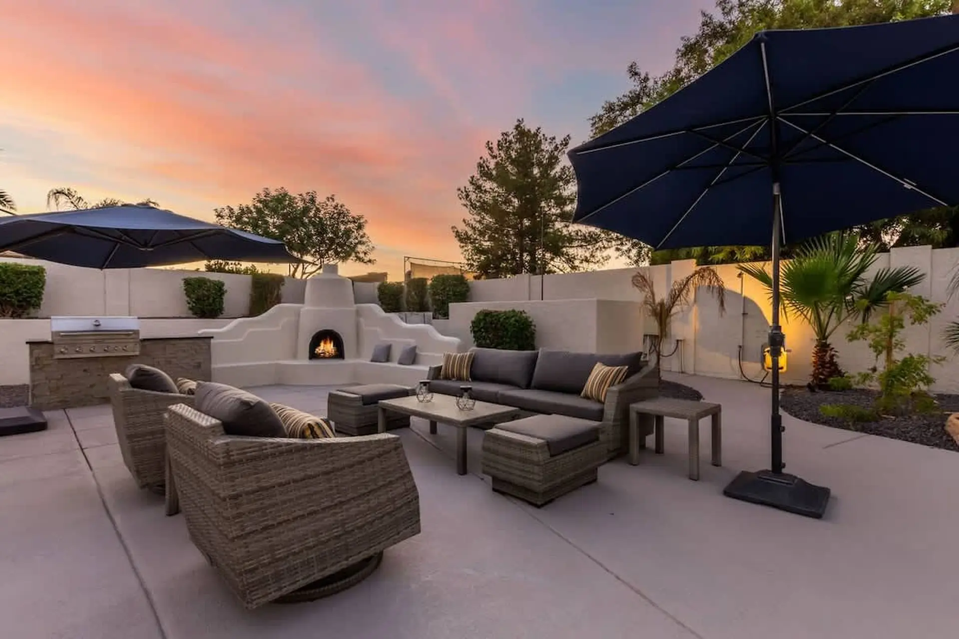An outdoor patio with furniture, a fireplace, and umbrellas at sunset.