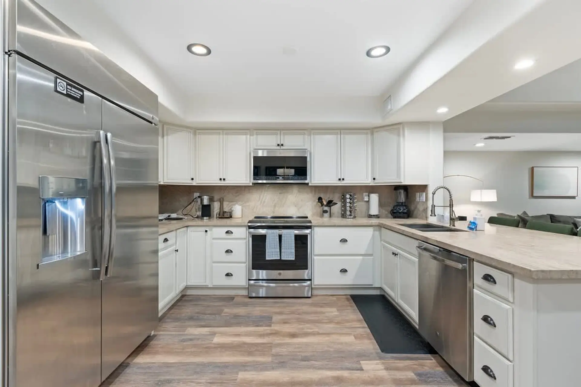 A stainless steel refrigerator stands in a modern kitchen with white cabinets and wood floors.