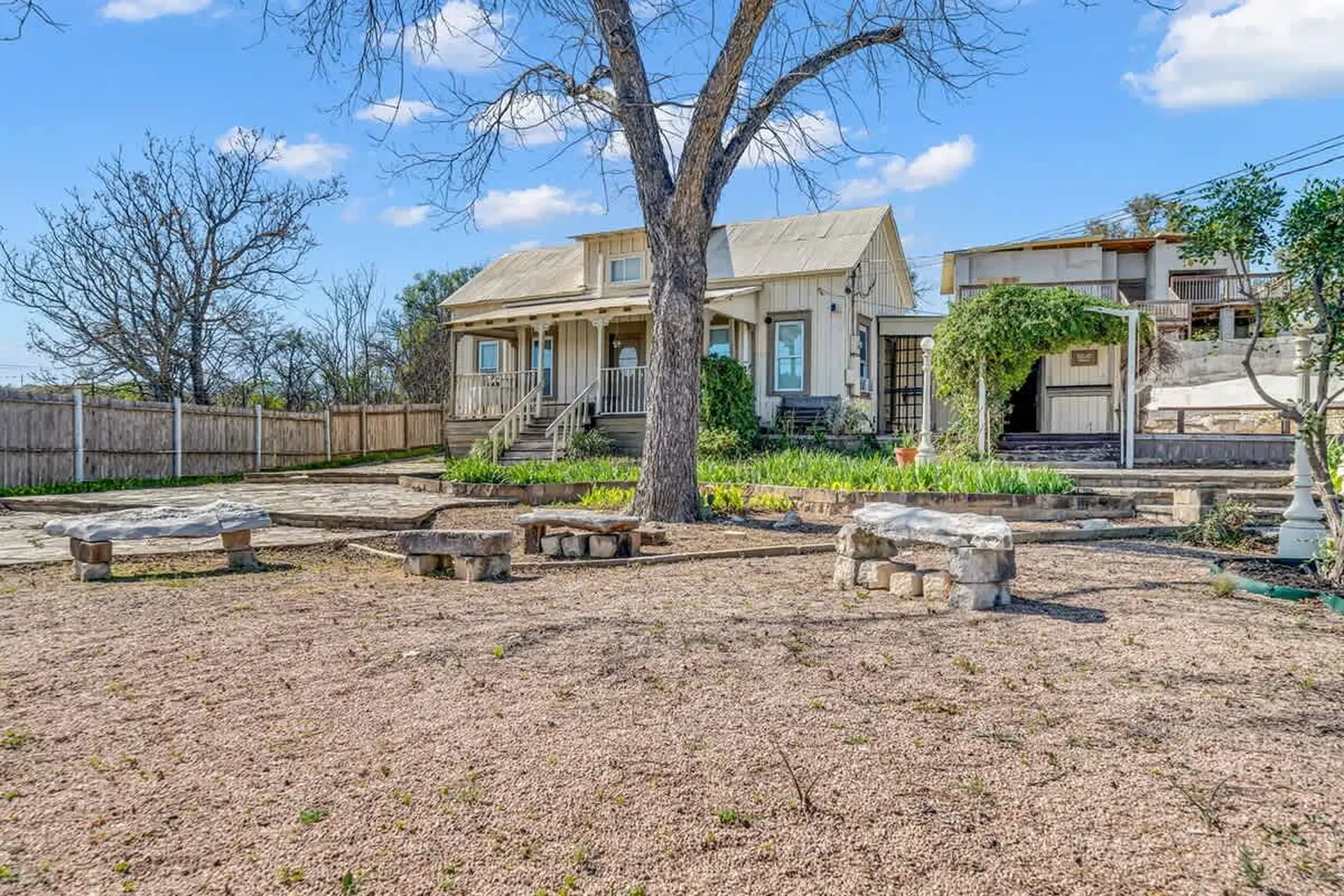 Outdoor scene with a house, a large tree, stone benches, and a gravel-covered yard.