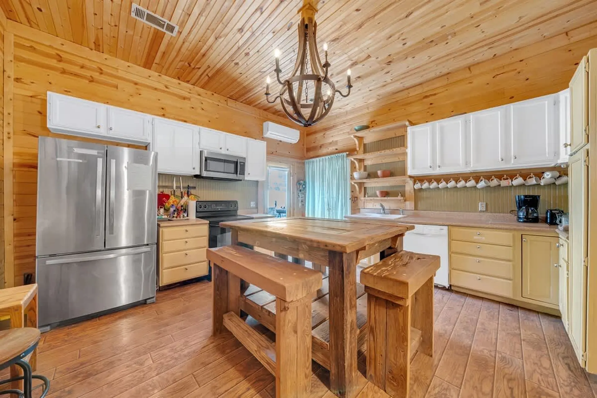 A rustic kitchen with wooden paneling, white cabinets, stainless steel appliances, and a wooden dini