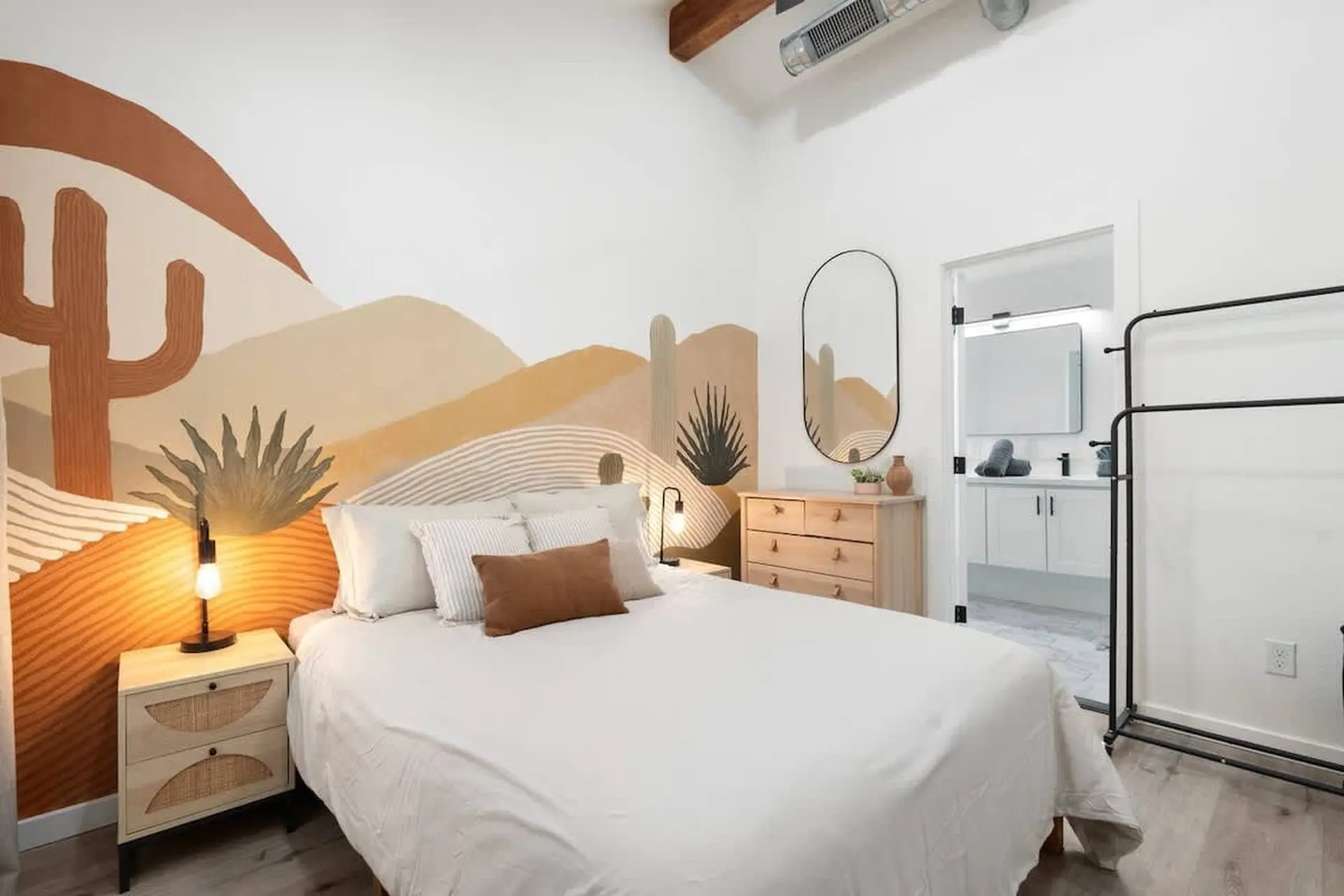 Bedroom with desert mural, white bedding, and a dresser with a mirror.