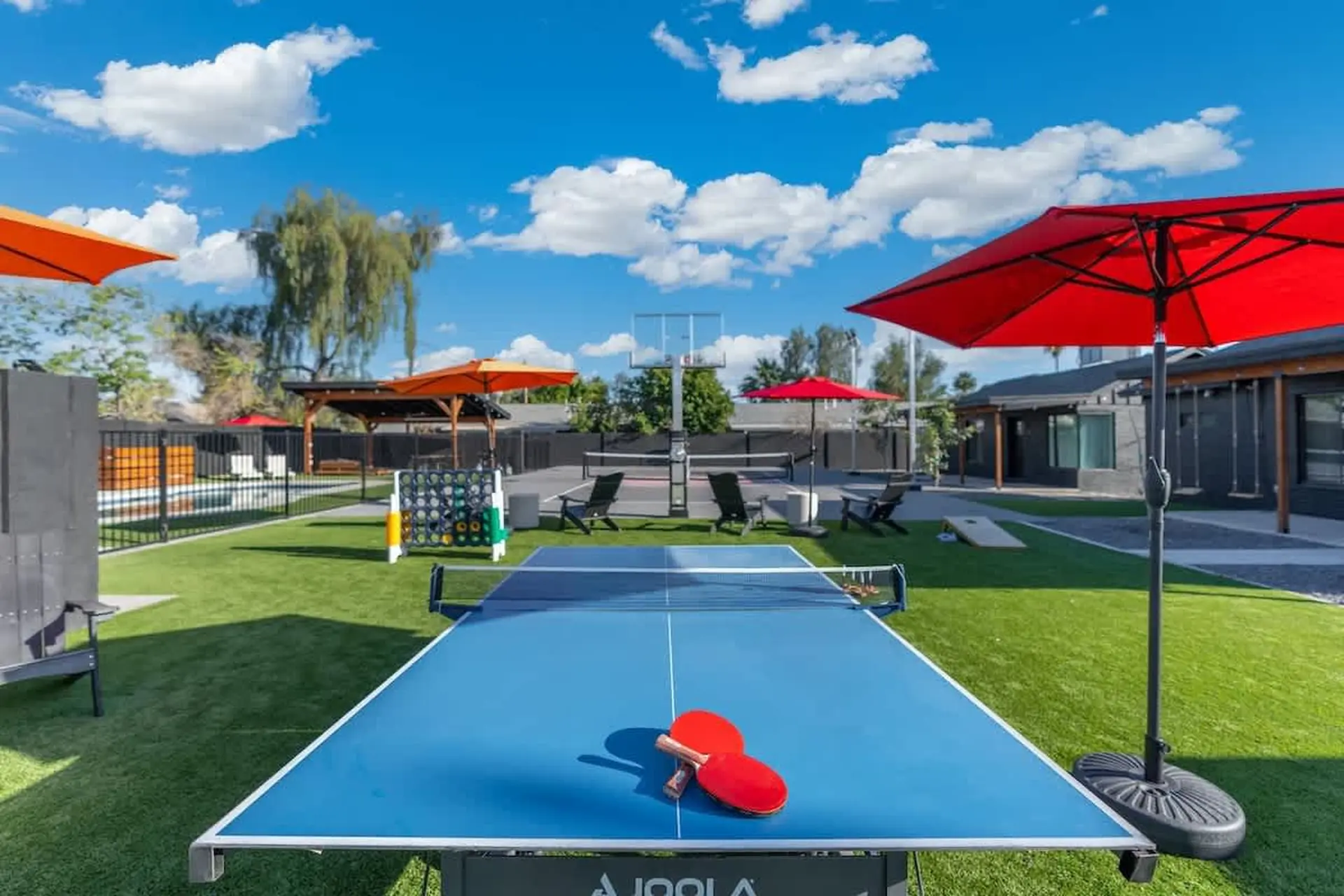 An outdoor recreational area with a ping pong table and red umbrellas.