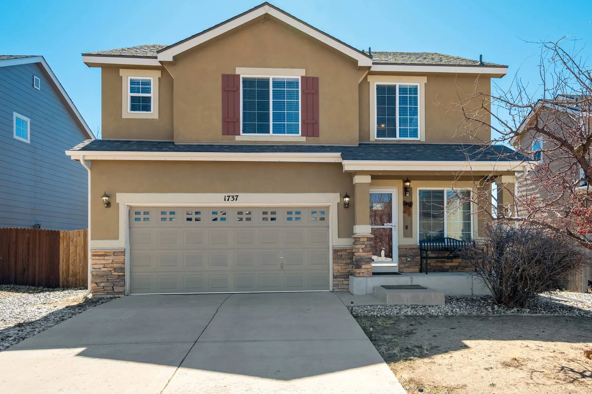 A tan two-story house with a beige garage door and a stone accent.