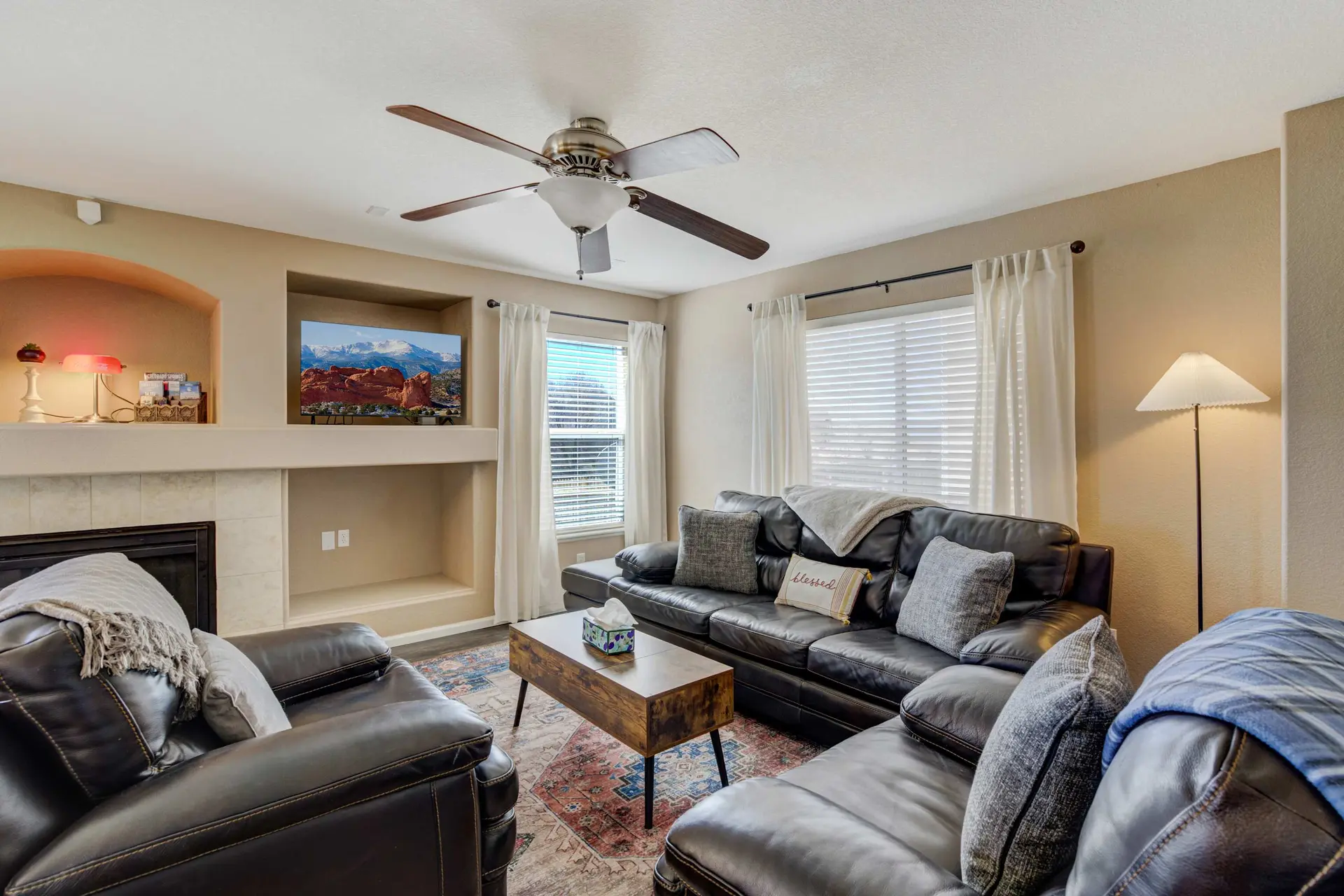 Living room with a dark leather sectional, coffee table, TV, and ceiling fan.