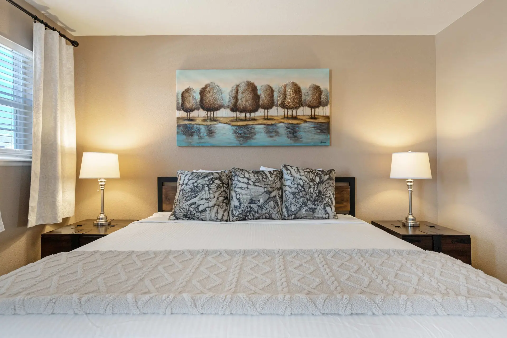 A bedroom with a bed, two lamps, and a painting.