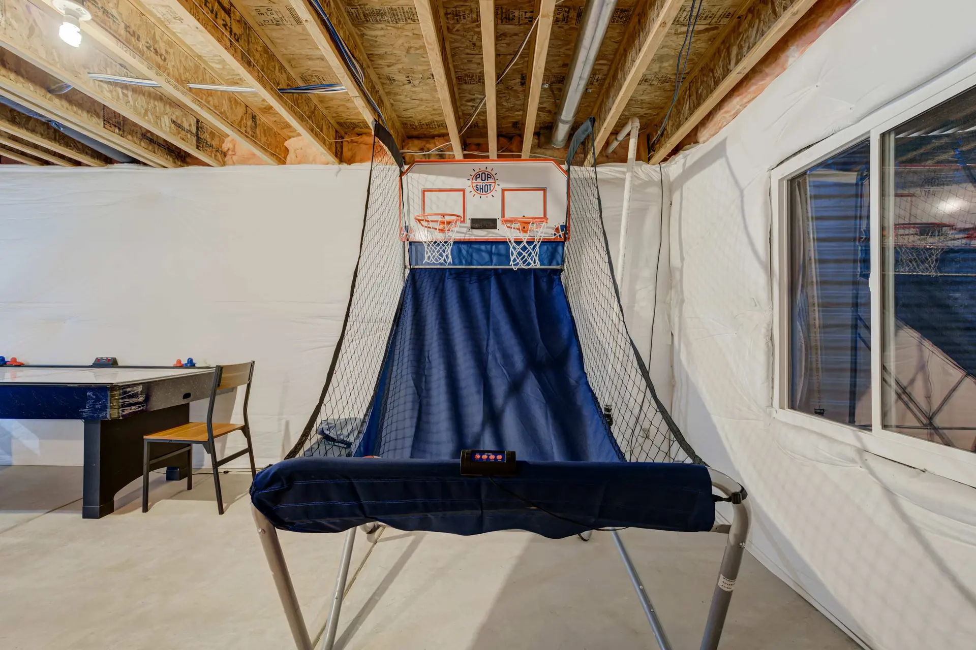 A basketball game is set up in a basement with a glass door and wood ceiling.