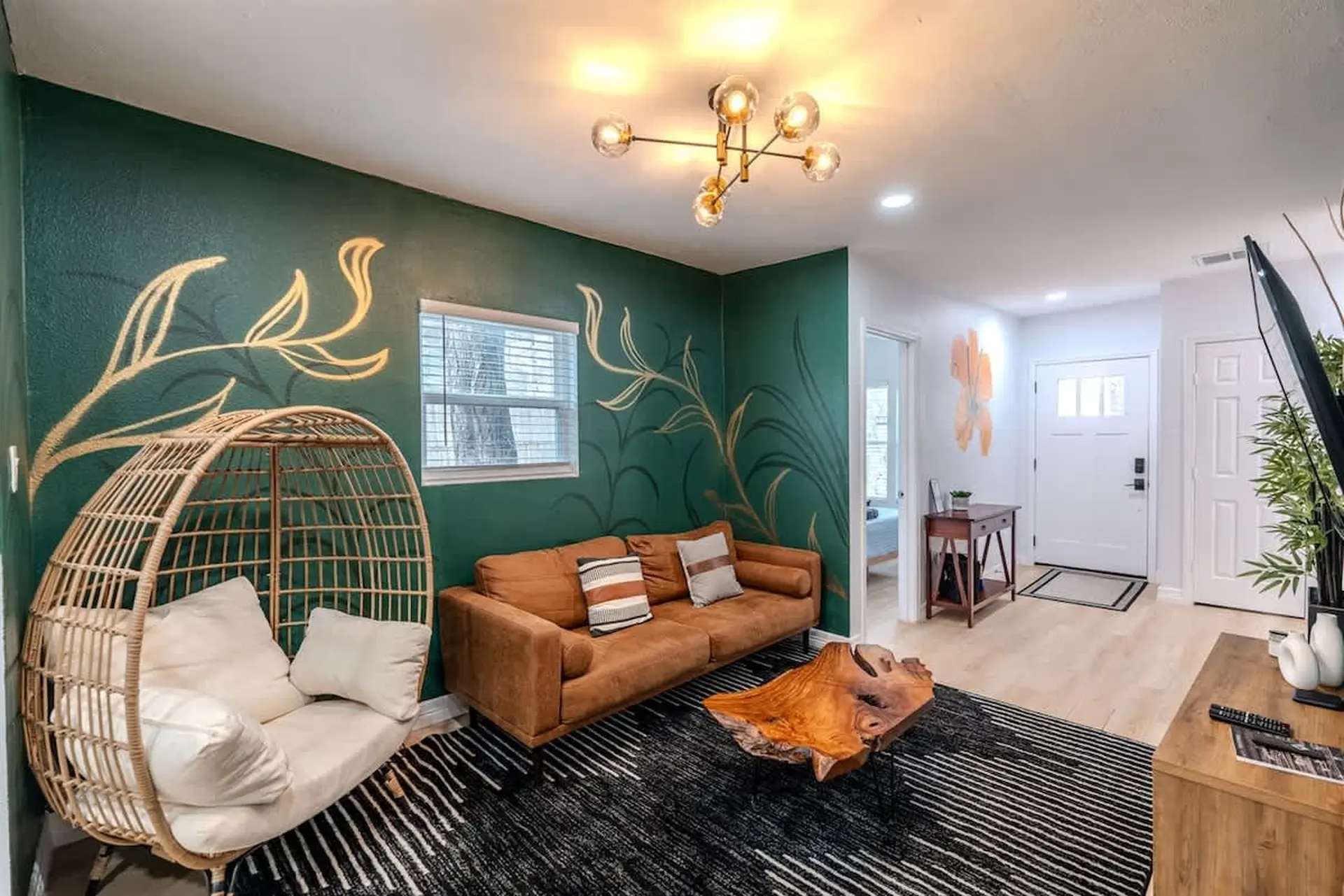 Living room with green accent wall, brown sofa, rattan chair, and wood coffee table.