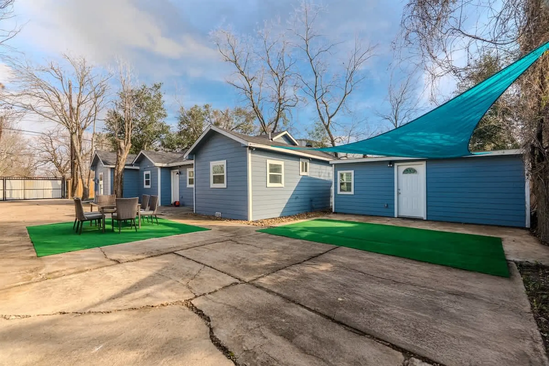 Blue cabins with tables and chairs are arranged on a concrete patio with artificial turf.