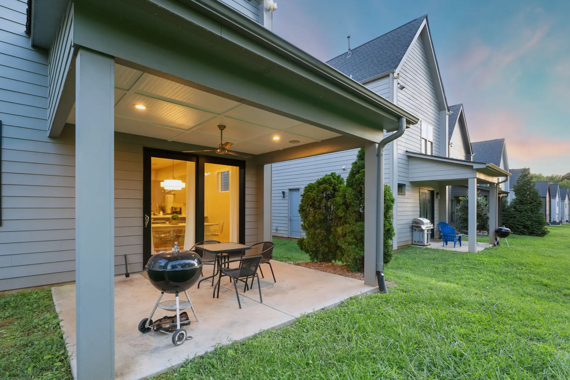 A covered patio with a grill and patio furniture sits outside a modern home.