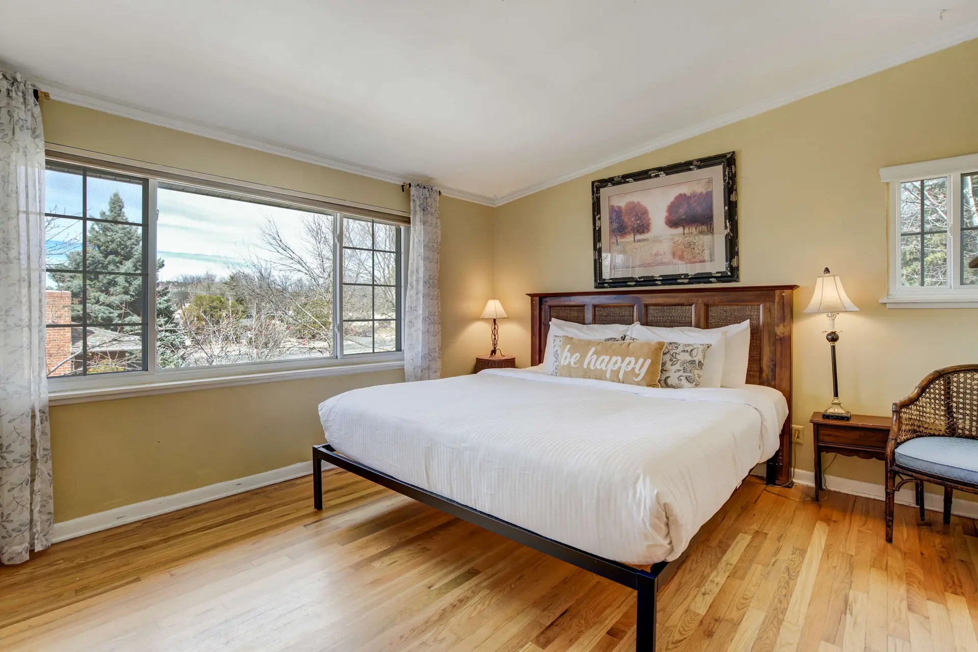 A king-size bed with white bedding sits in a bedroom with wood floors and yellow walls.