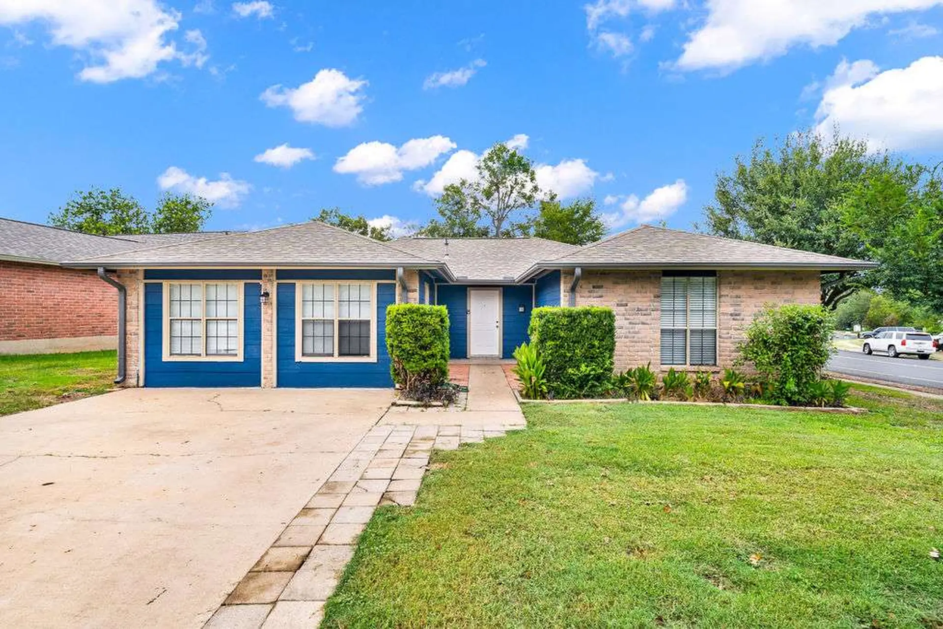 A bright blue house with a brick accent and a lush green lawn under a cloudy blue sky.