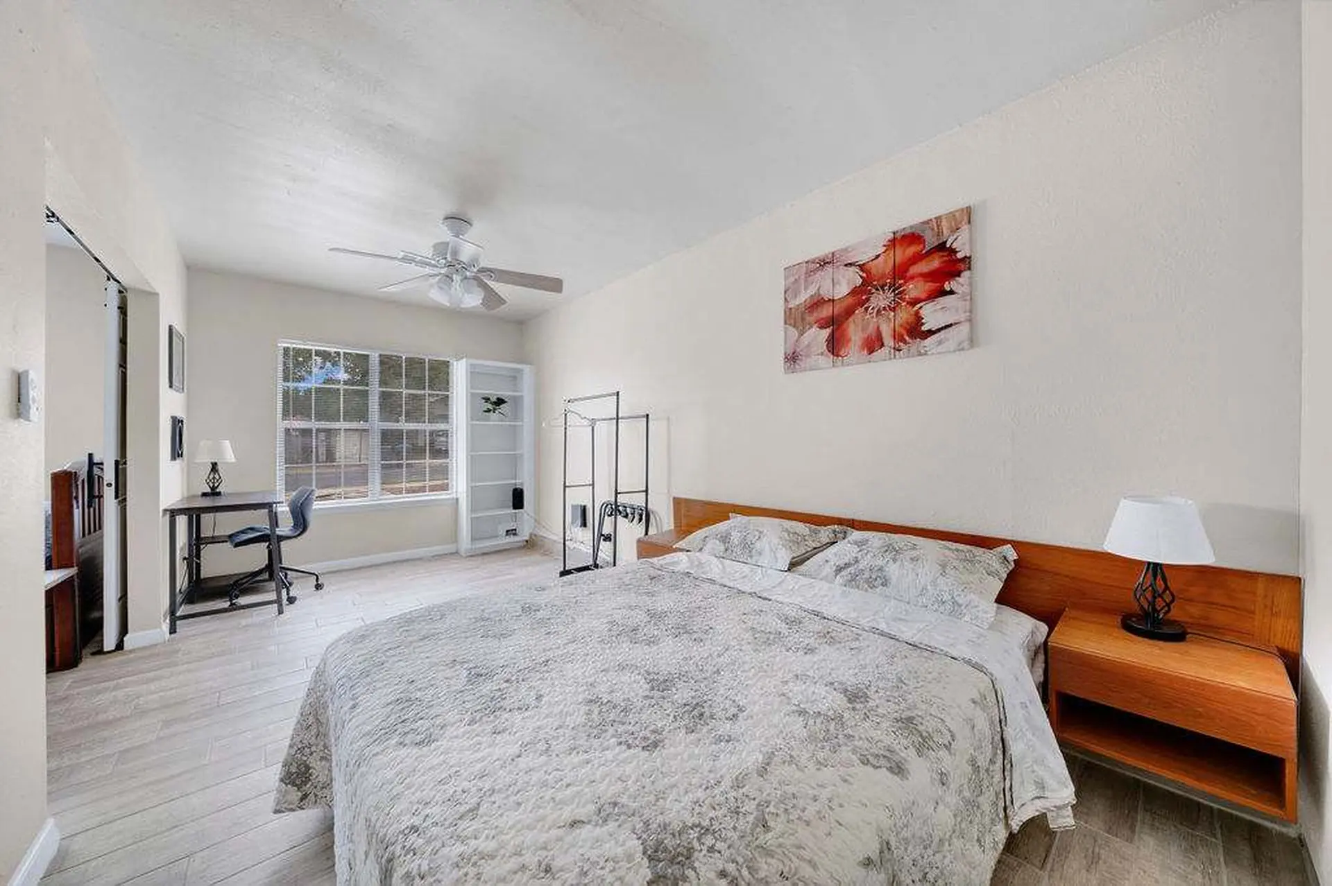 A bedroom with a bed, desk, and a floral painting on the wall.