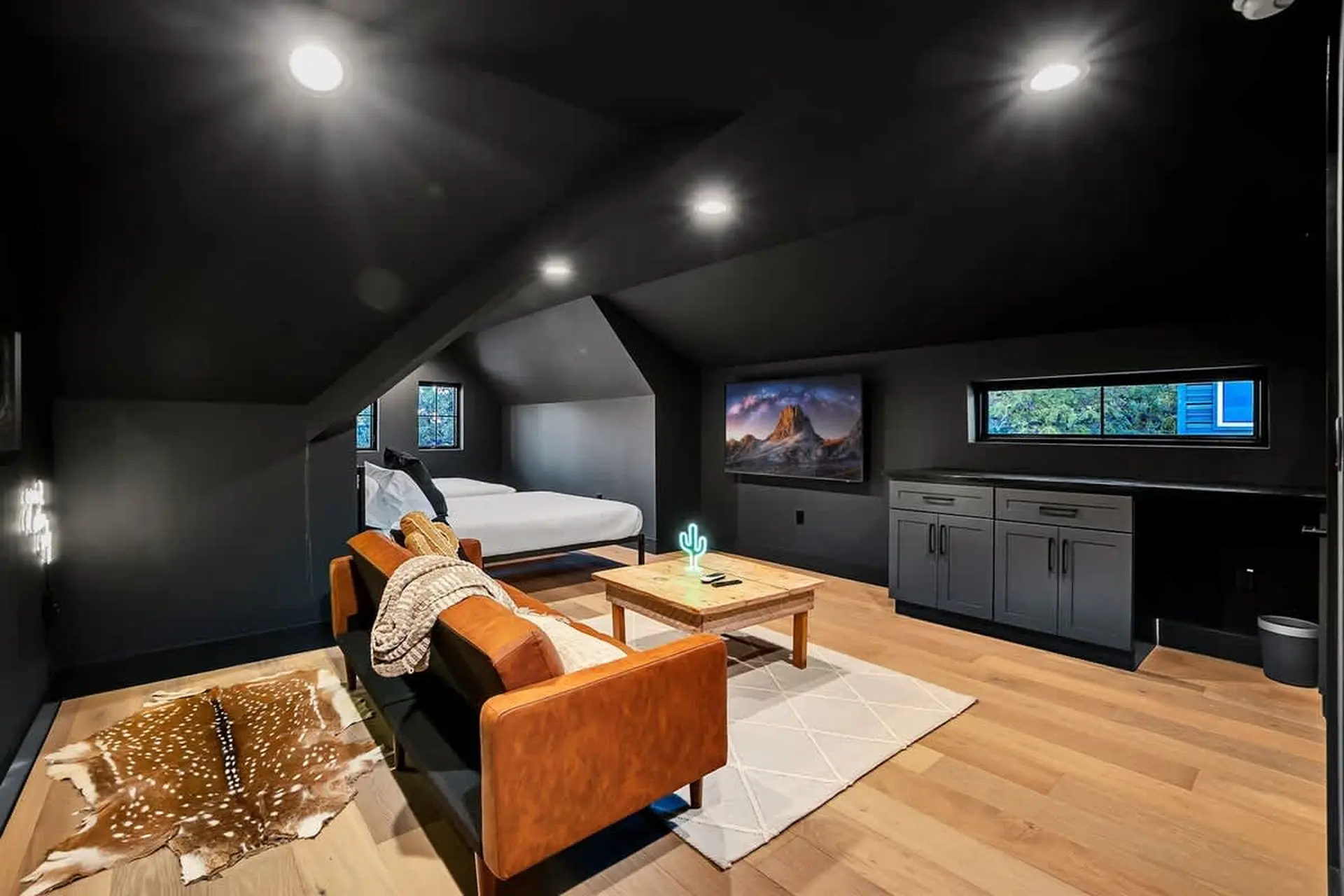 A rustic attic living space with a brown leather sofa, deer hide rug, and a tv.