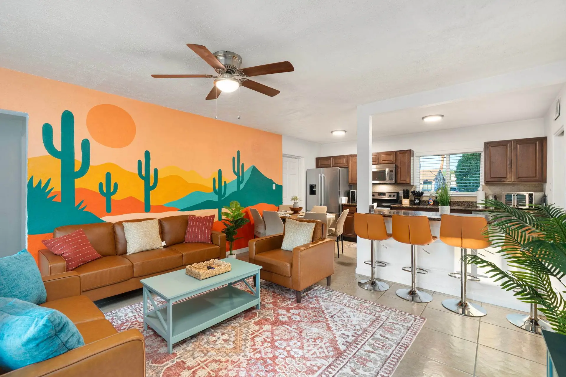 A living room with a desert mural, brown leather sofas, and a kitchen with bar stools.