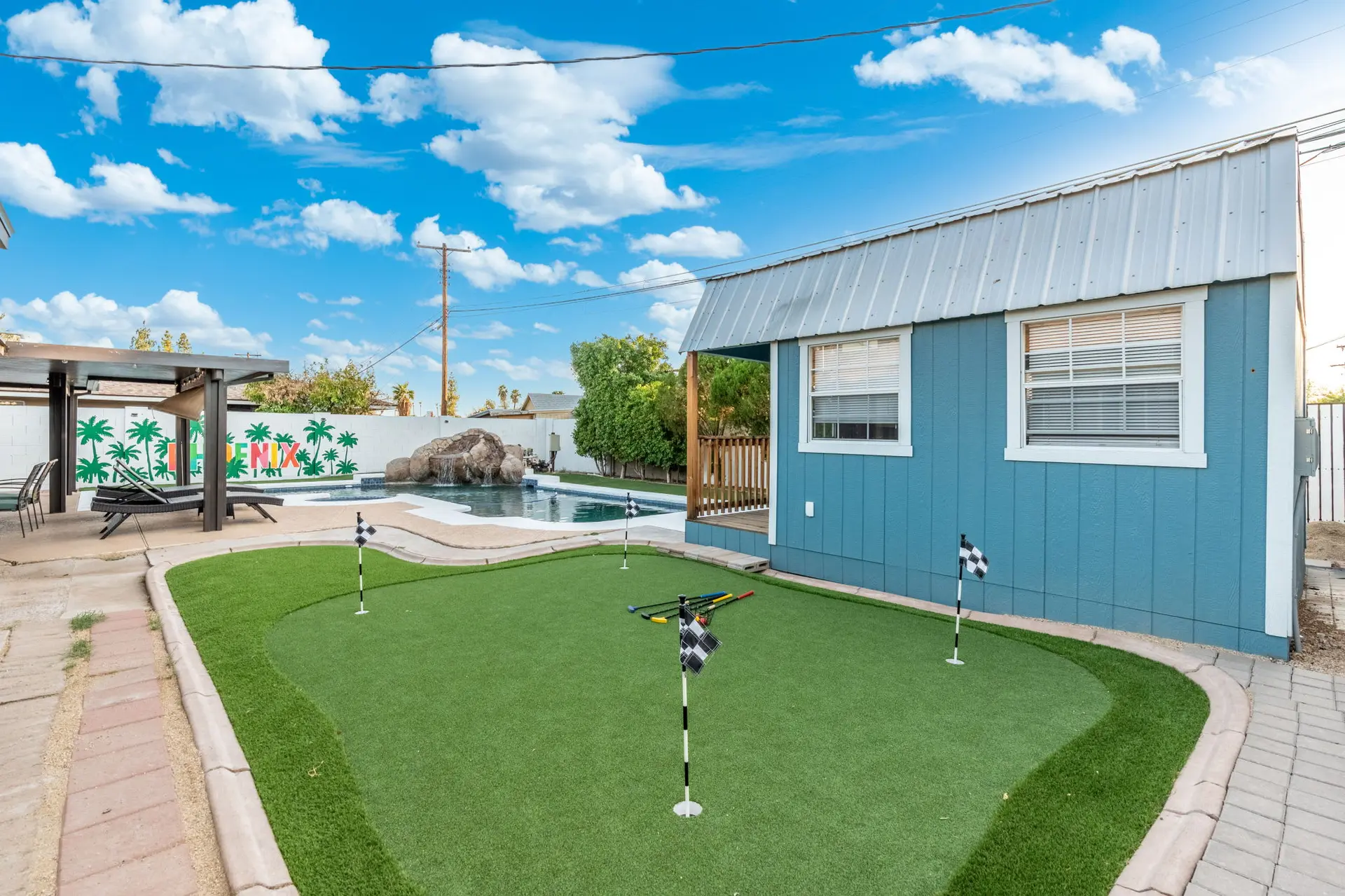 Backyard with putting green, pool with waterfall, and blue shed.