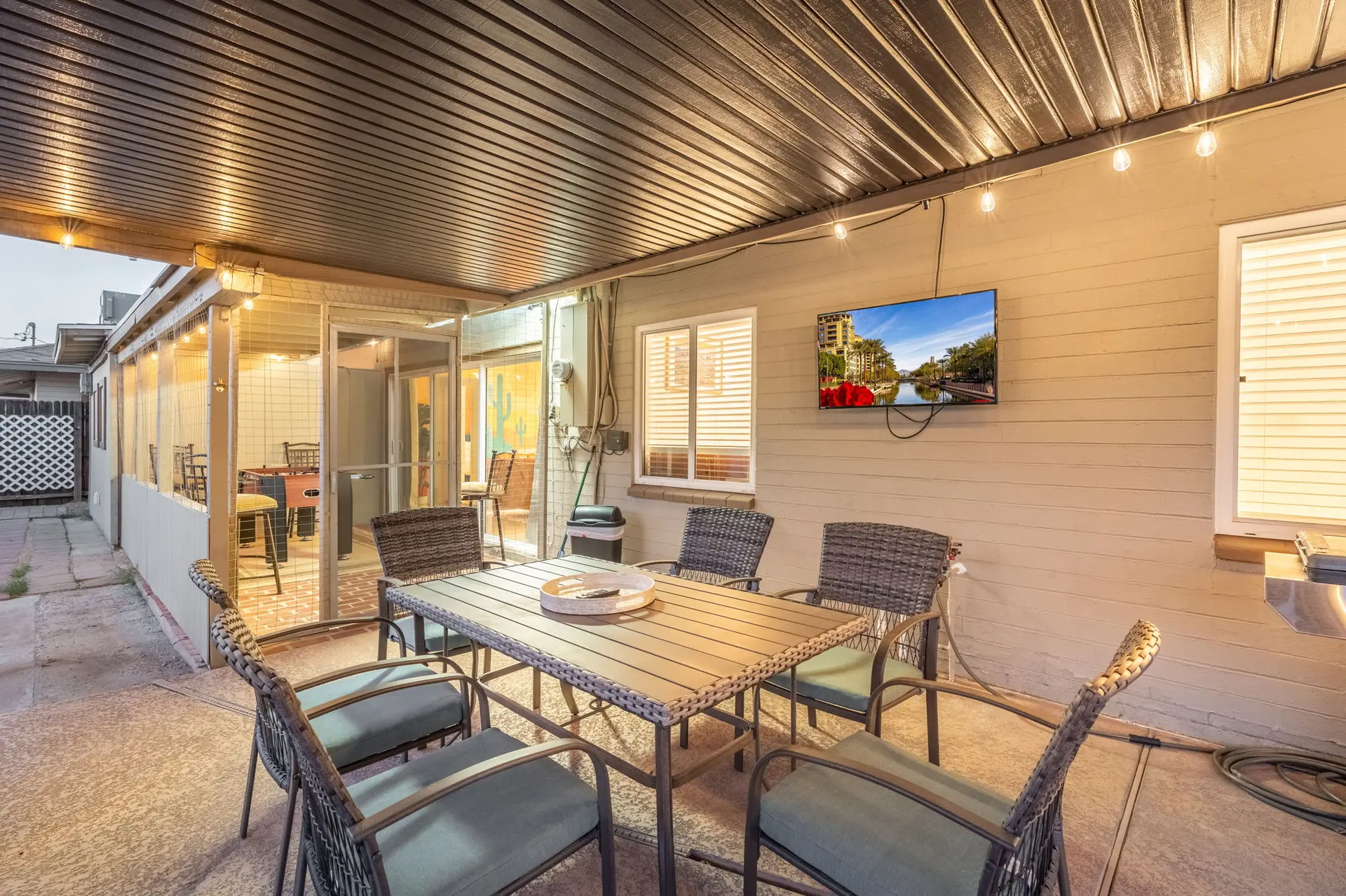 A covered patio with a dining table, chairs, and a television.
