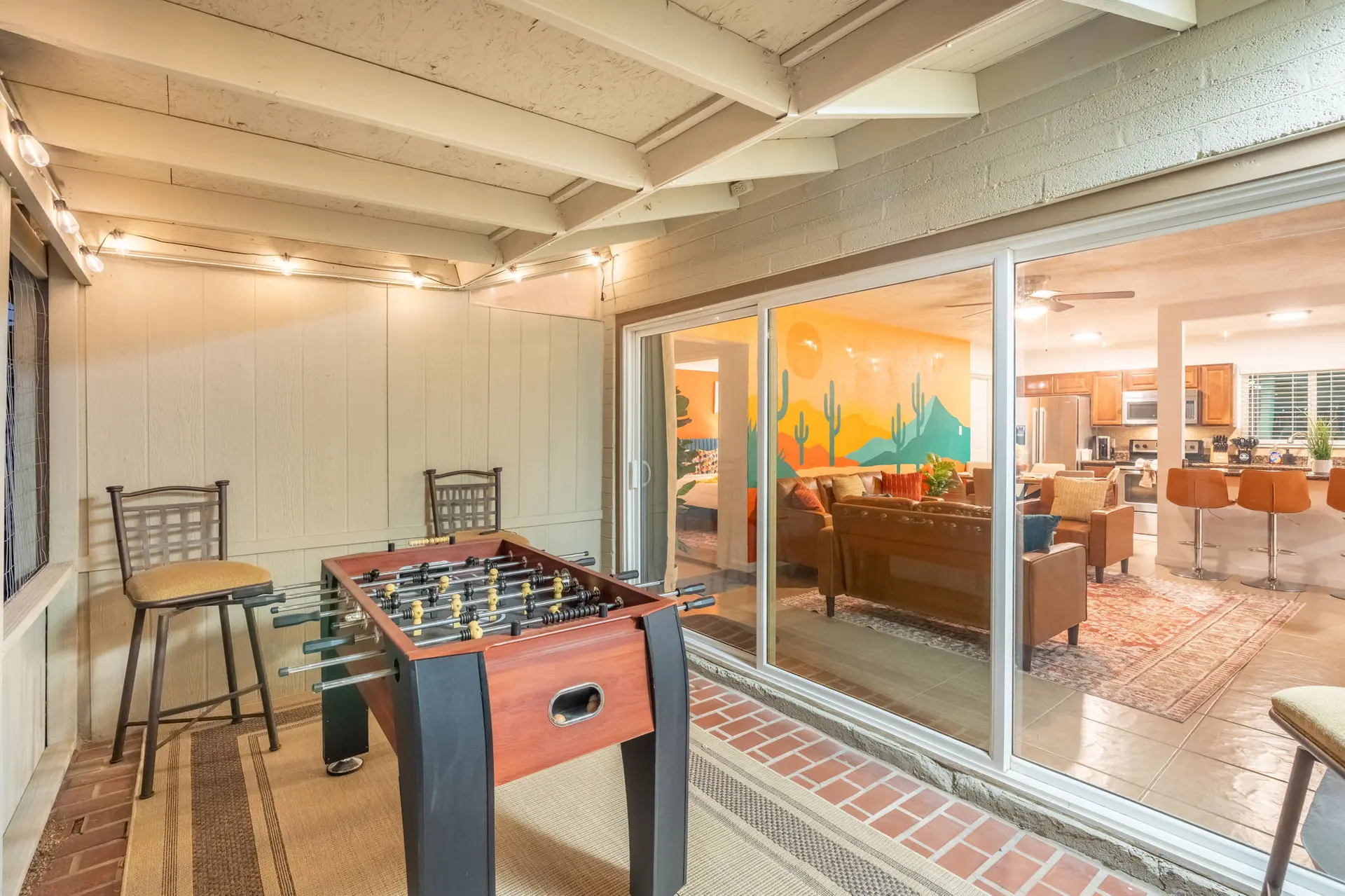 A foosball table and bar stools are on a patio with string lights.