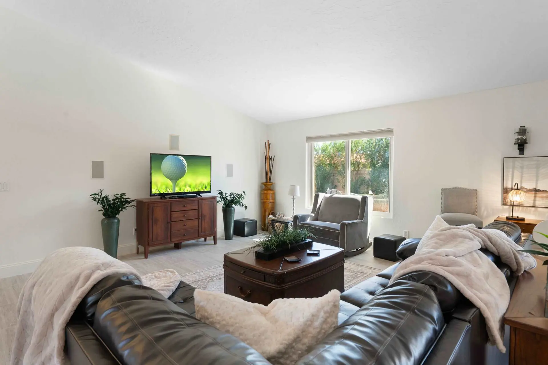 A living room with a dark leather sectional, large coffee table trunk, TV, and a large window.