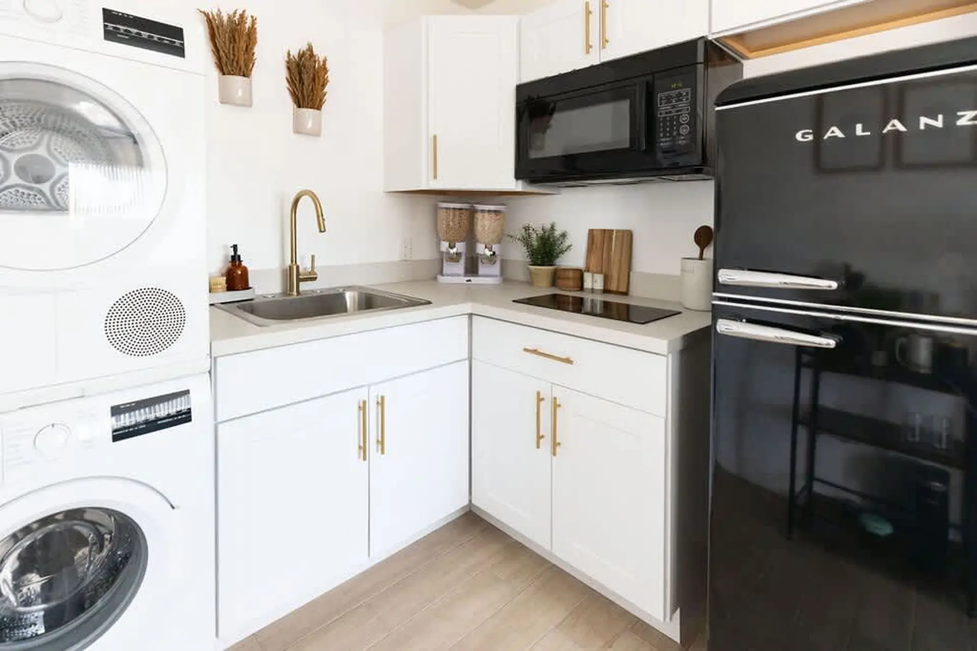 A small, modern kitchen with white cabinets, a black refrigerator and microwave, and a washer and dr