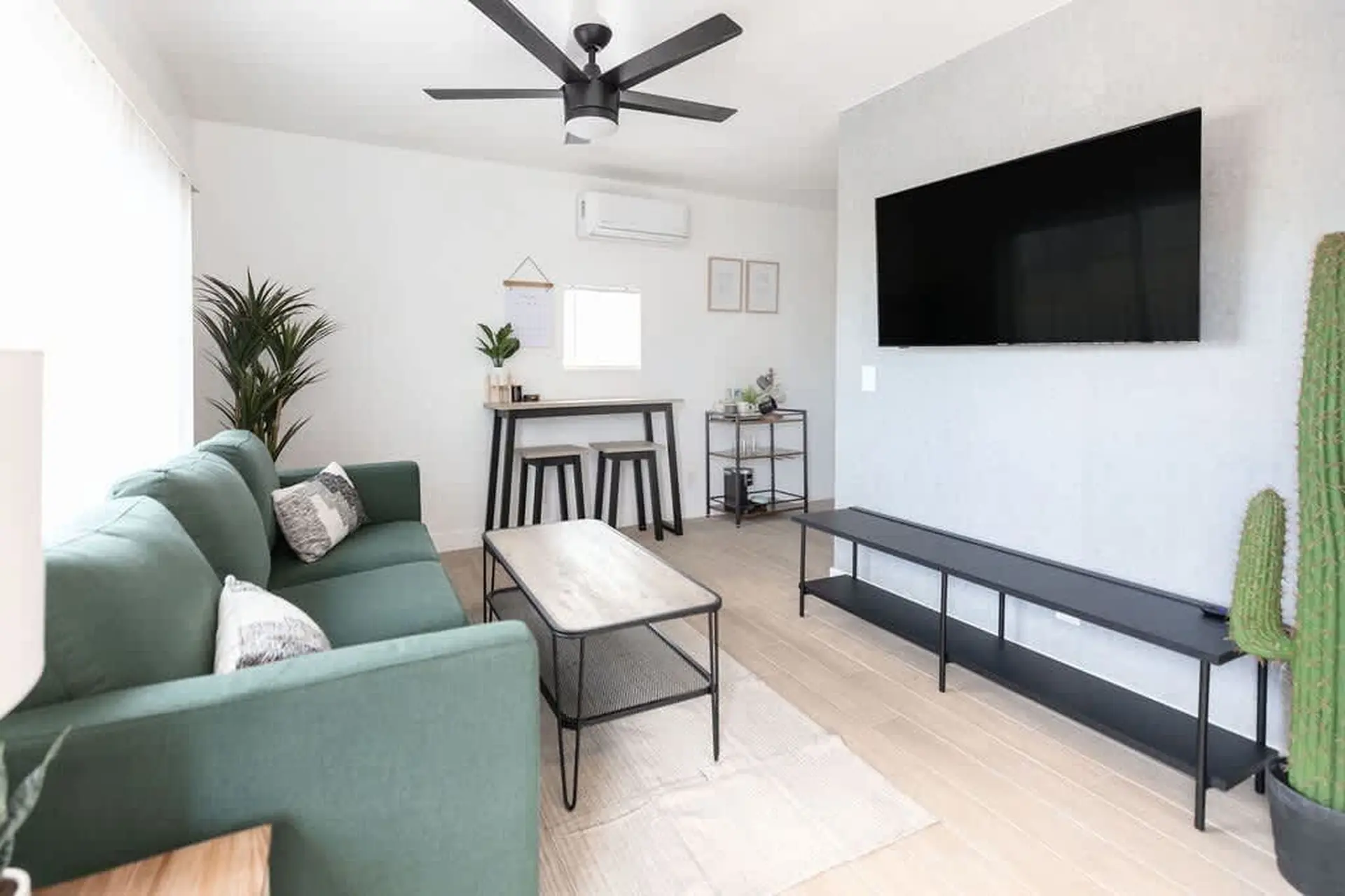 A modern living room with a green sofa, coffee table, TV, and ceiling fan.
