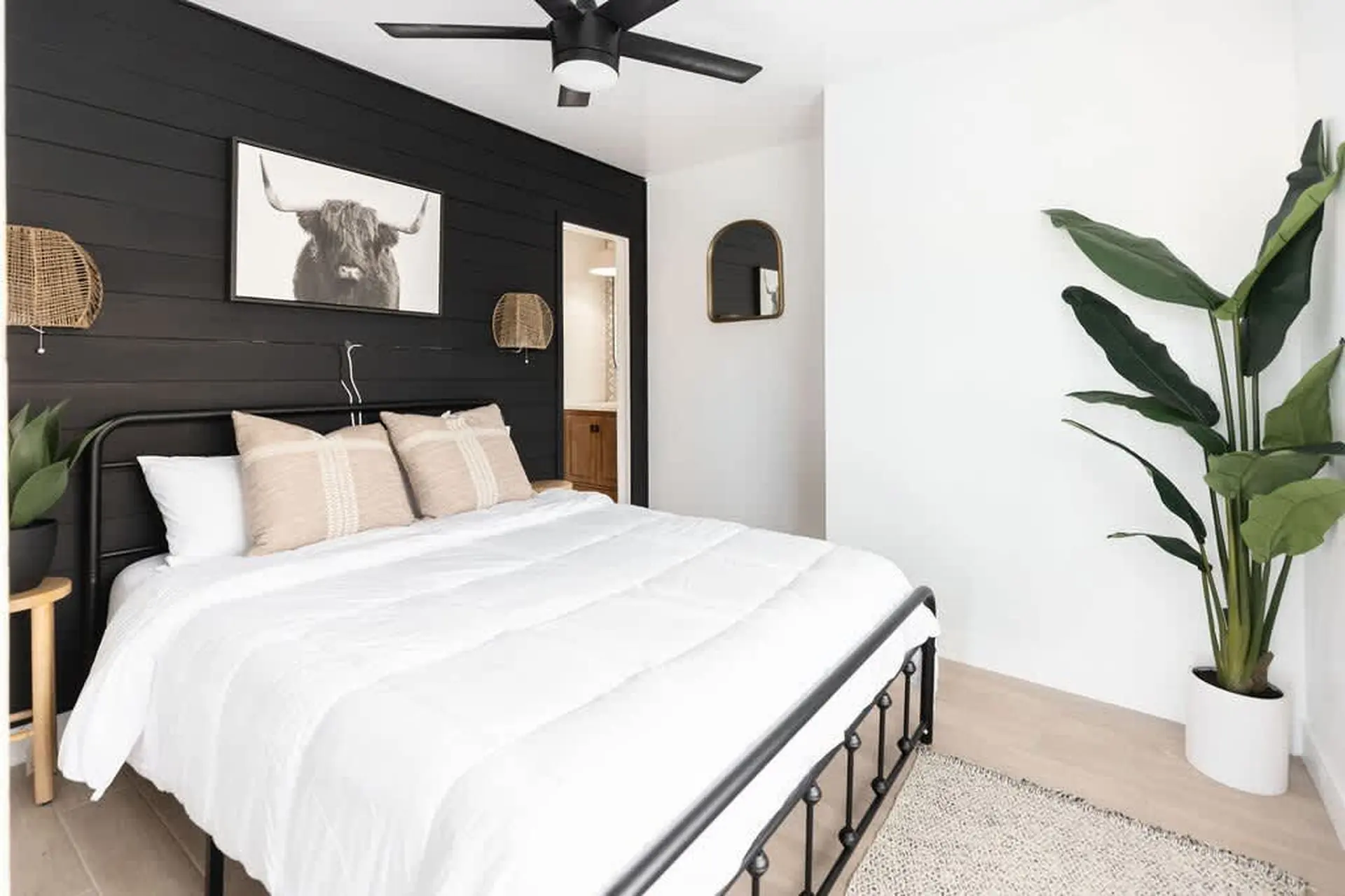 A modern bedroom with a black accent wall, a bull head painting, and a white bed.