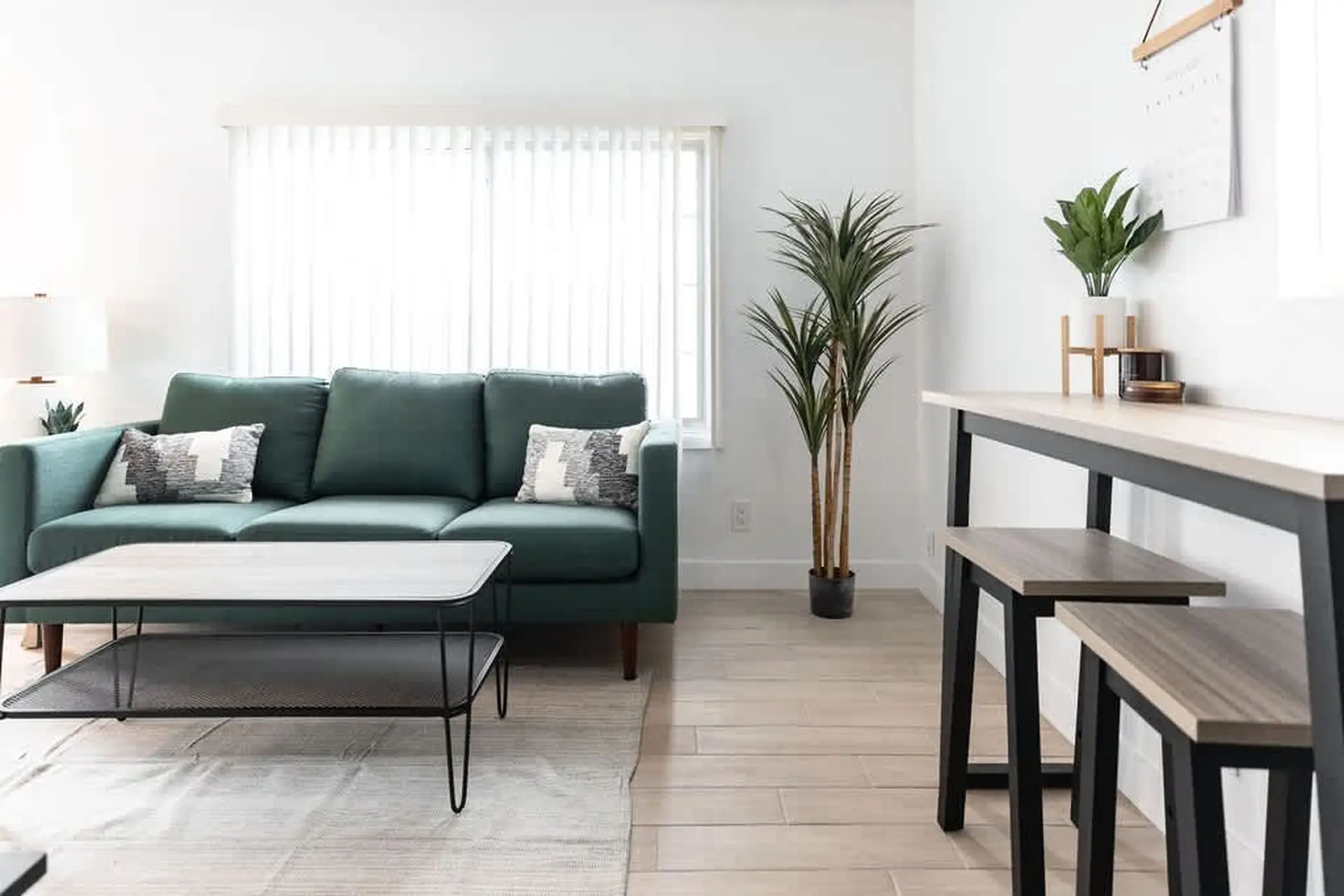 A stylish living room with a teal sofa, coffee table, and dining area with stools.