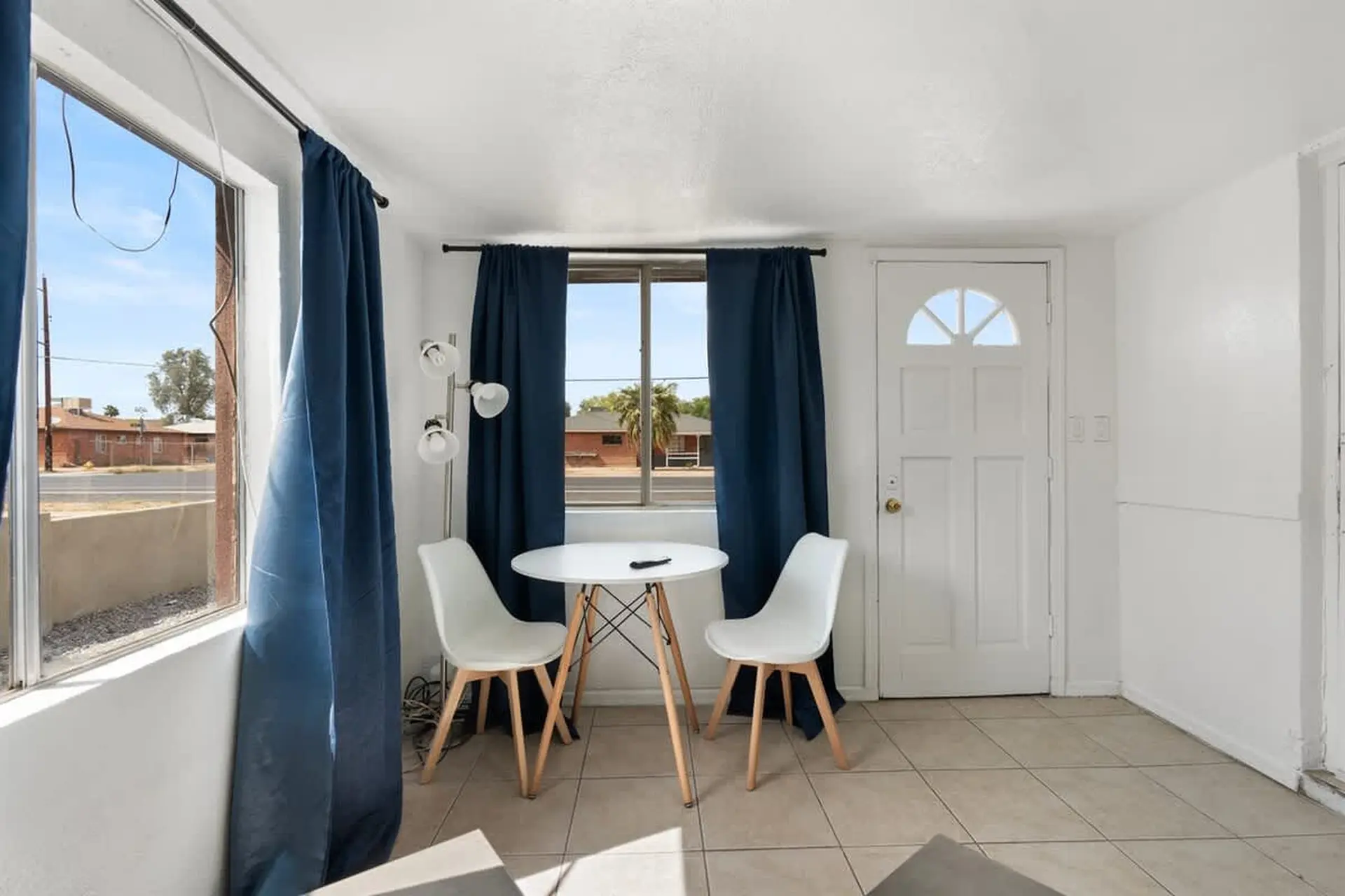 A small dining table with two chairs sits in front of a window, next to a white door.