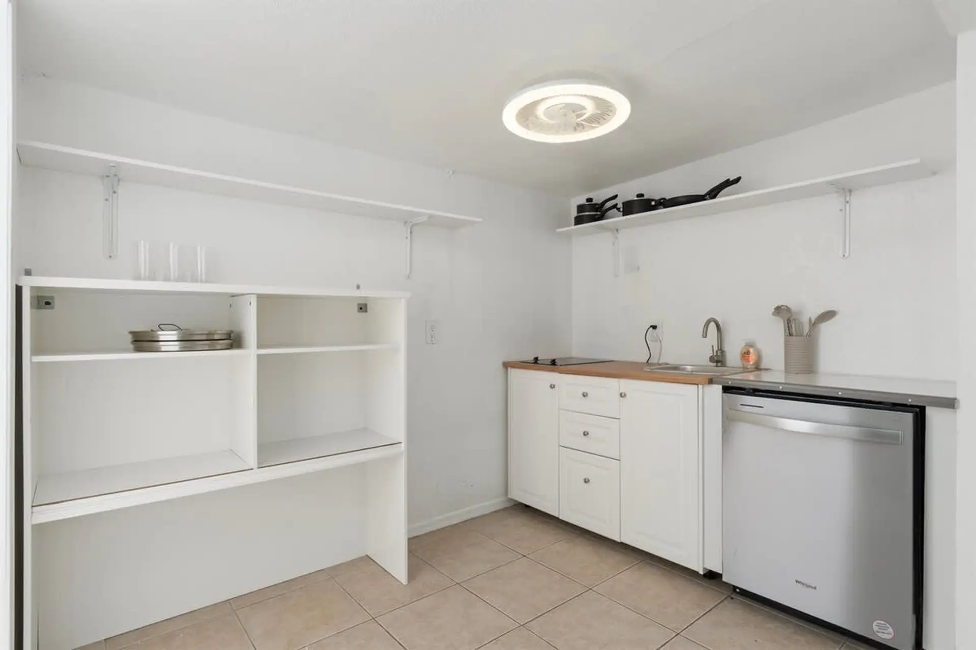 A clean, white kitchen with cabinets, a sink, dishwasher, and shelving.