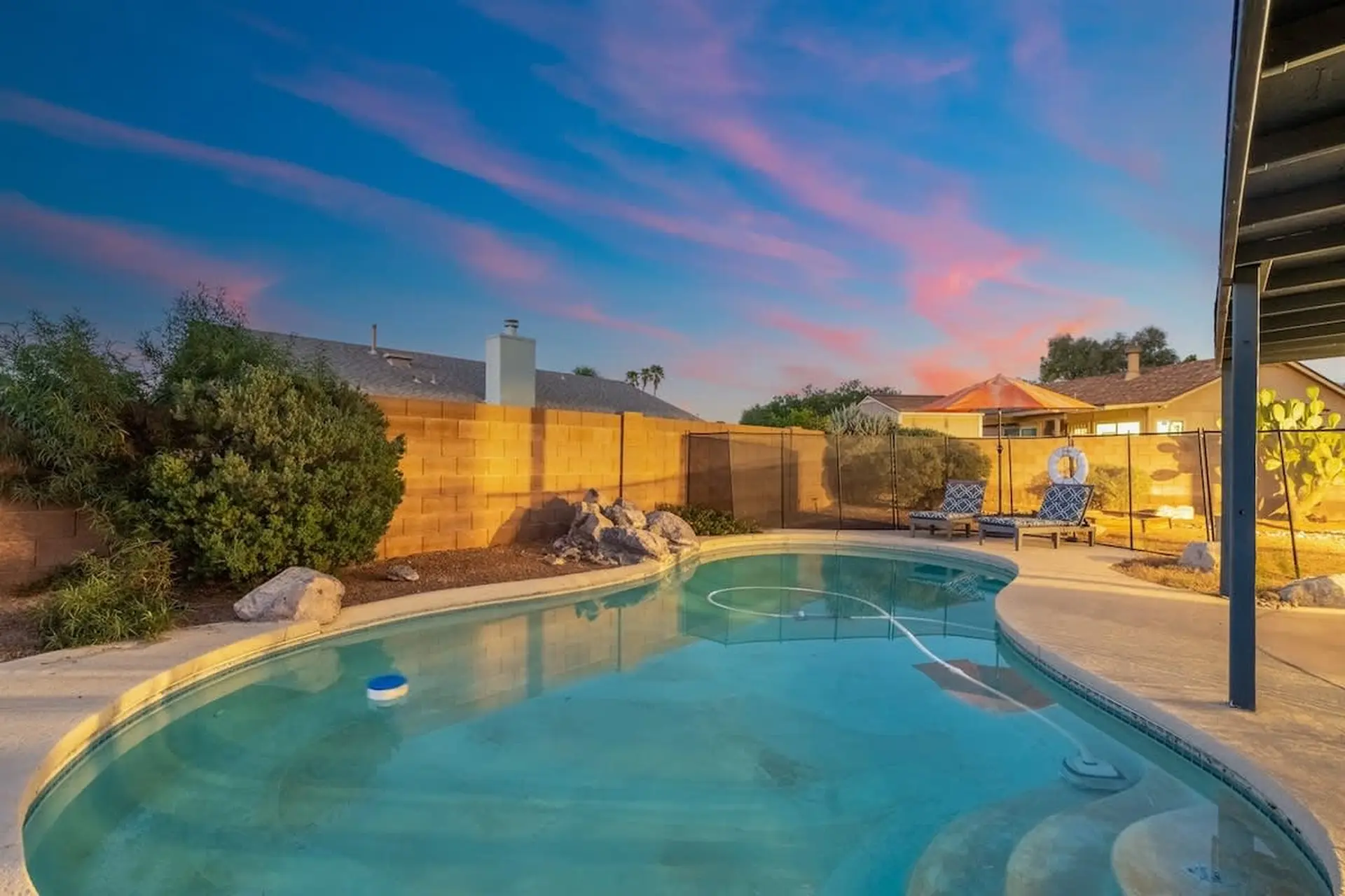 Backyard swimming pool at sunset with lounge chairs and a brick wall.