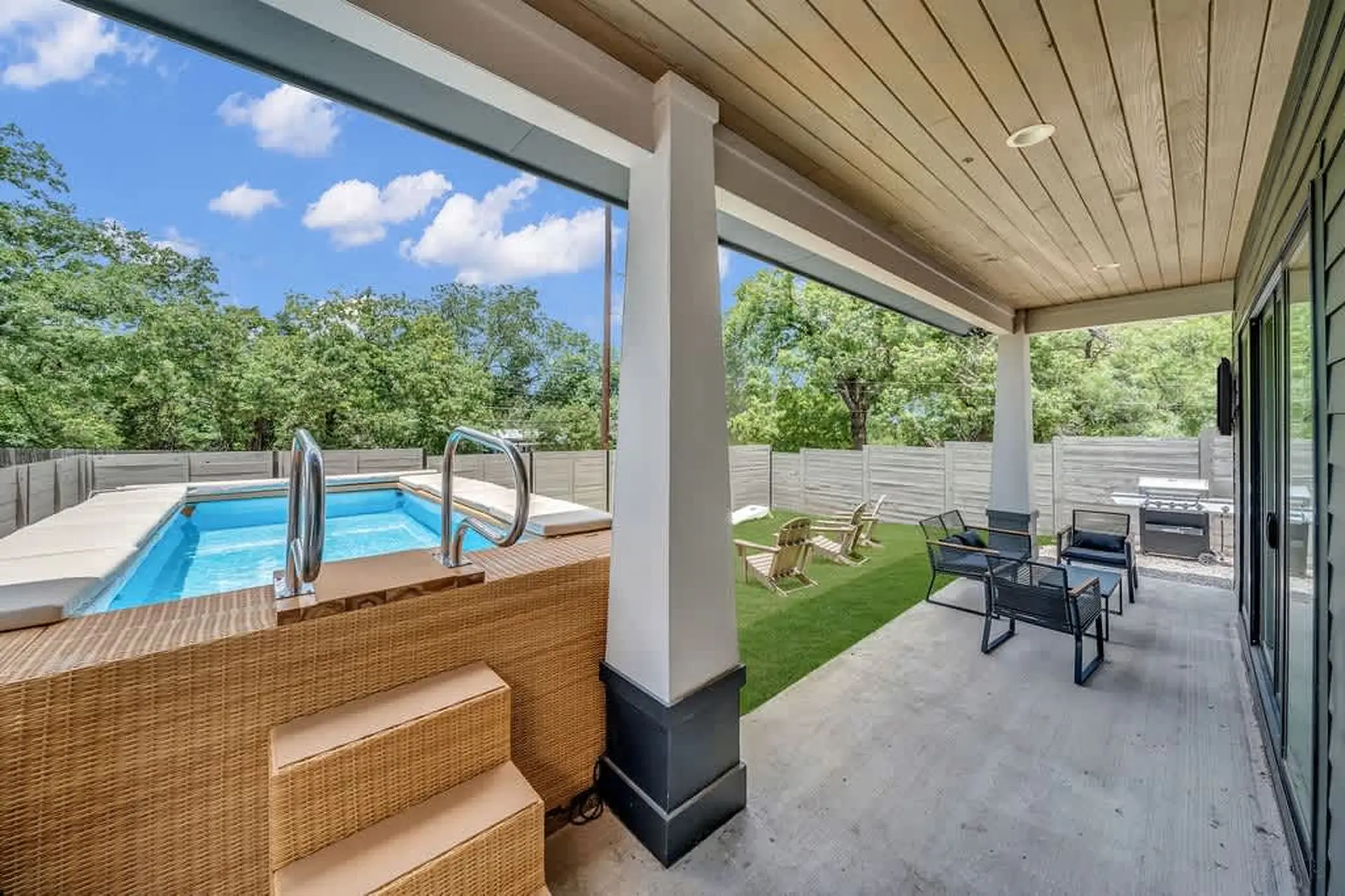 A covered patio with a pool, seating, and a grill.