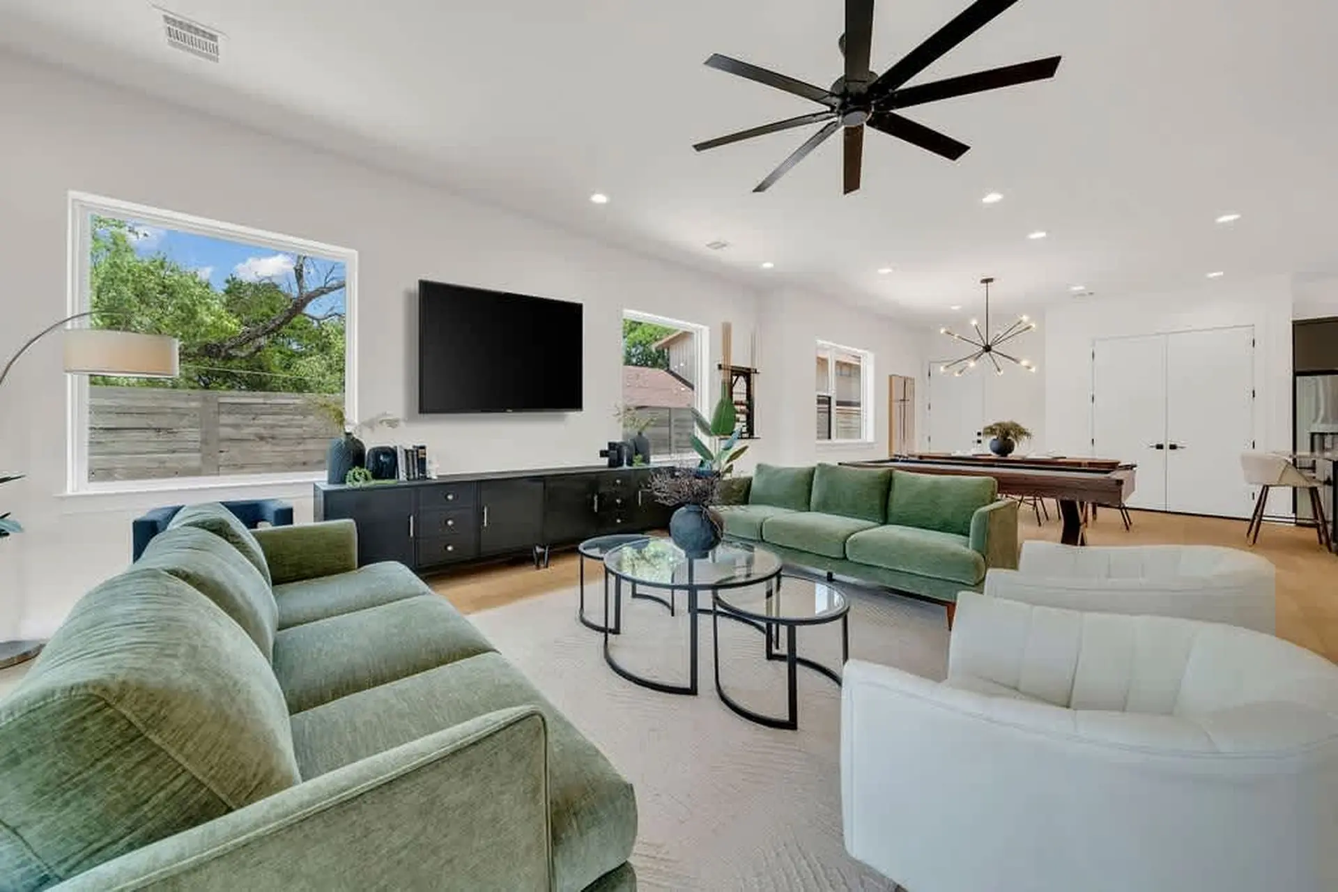 A modern living room with green sofas, a pool table, and a ceiling fan.