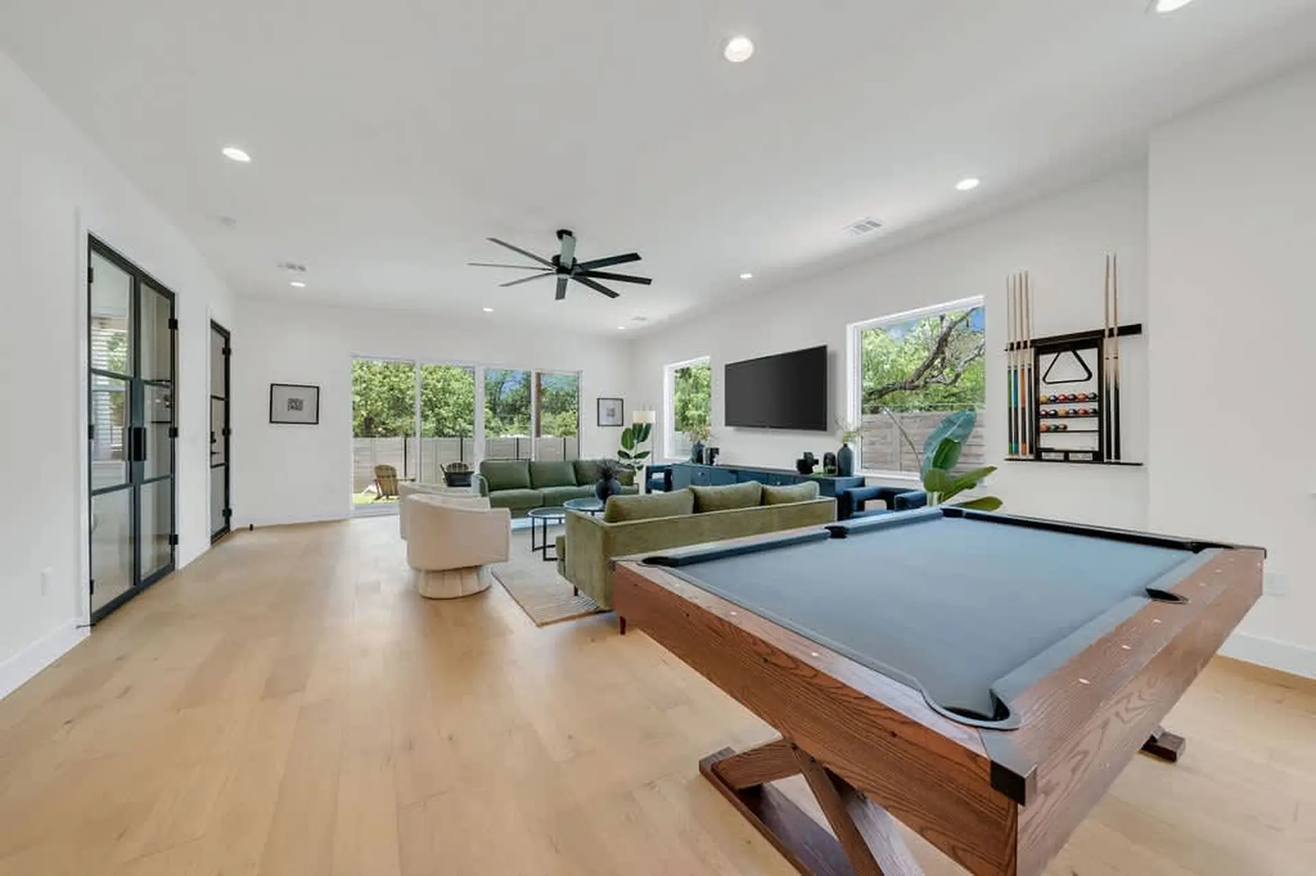 Living room with a pool table, green sofas, and large windows.