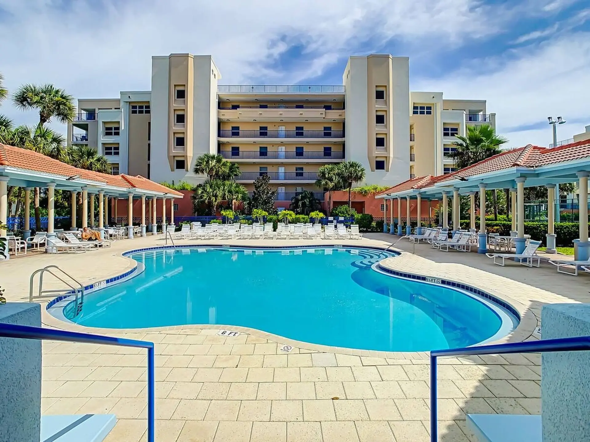 Resort pool with lounge chairs, palm trees, and a modern hotel.