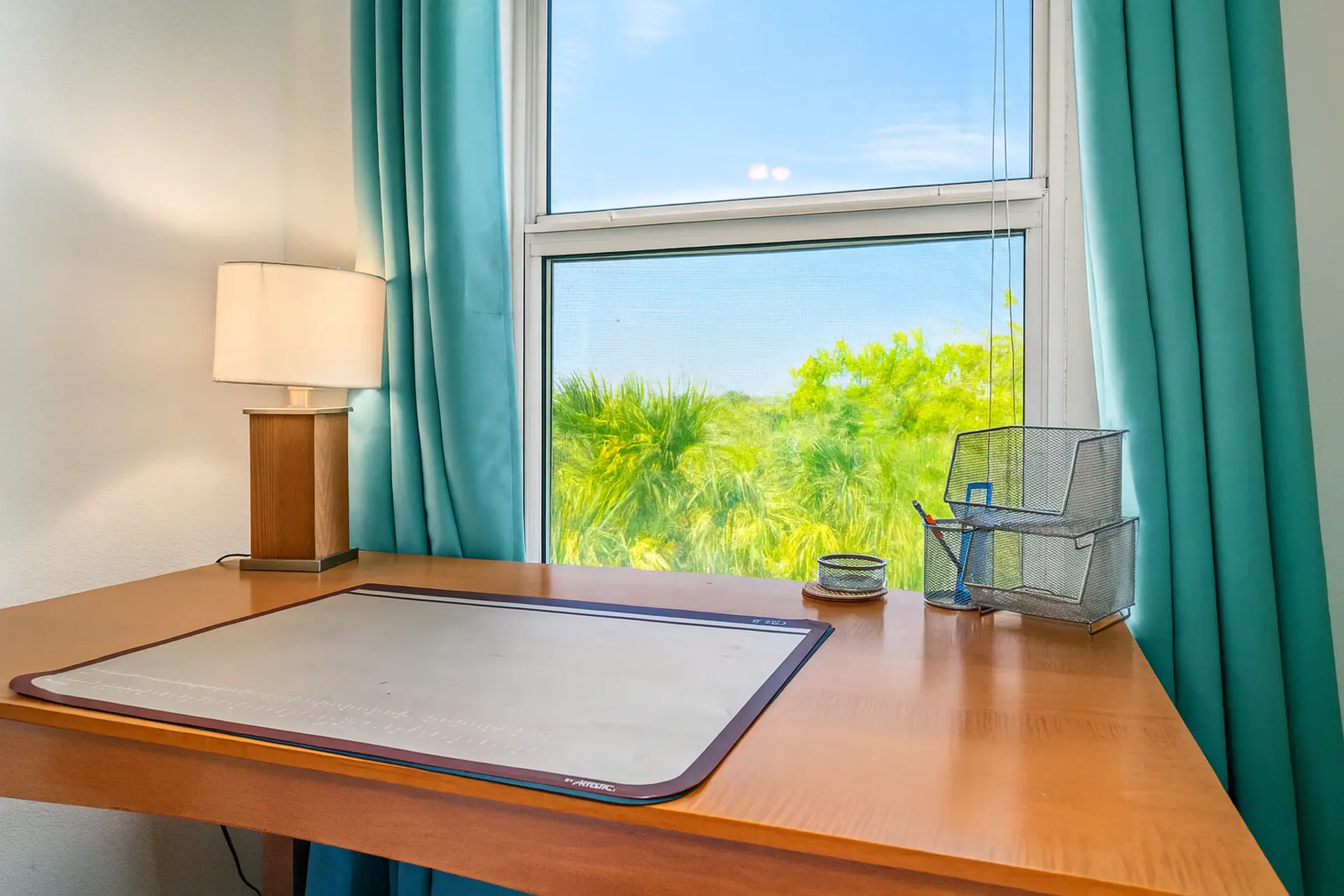Desk with lamp, cutting mat, and storage baskets in front of a sunny window.