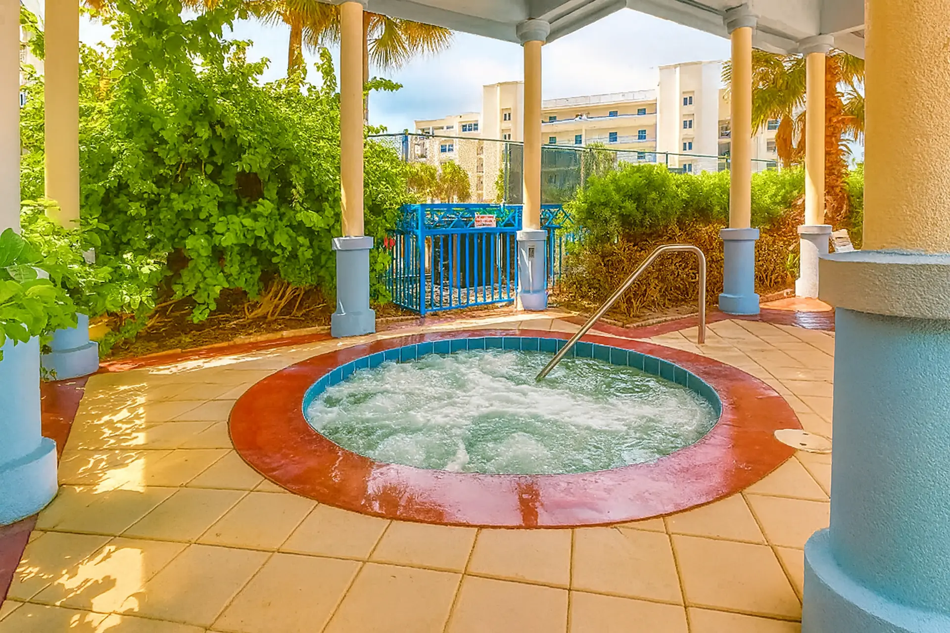 A bubbling hot tub sits on a tiled patio, surrounded by lush greenery and palm trees.