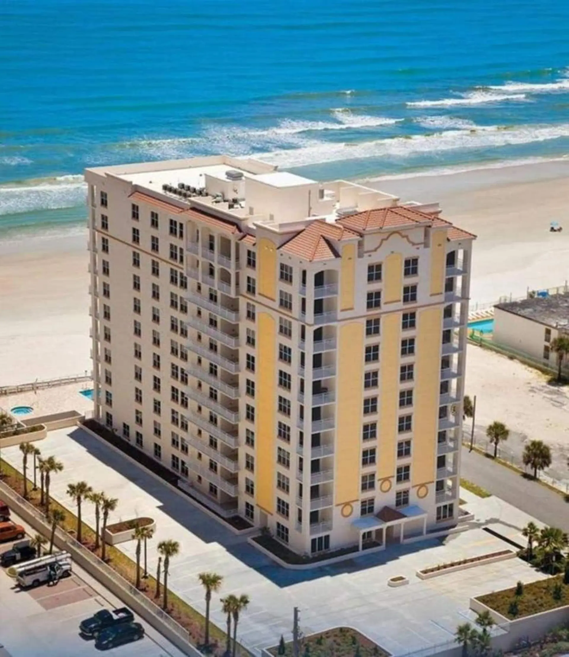 A tall hotel with balconies sits on a beach next to the ocean.