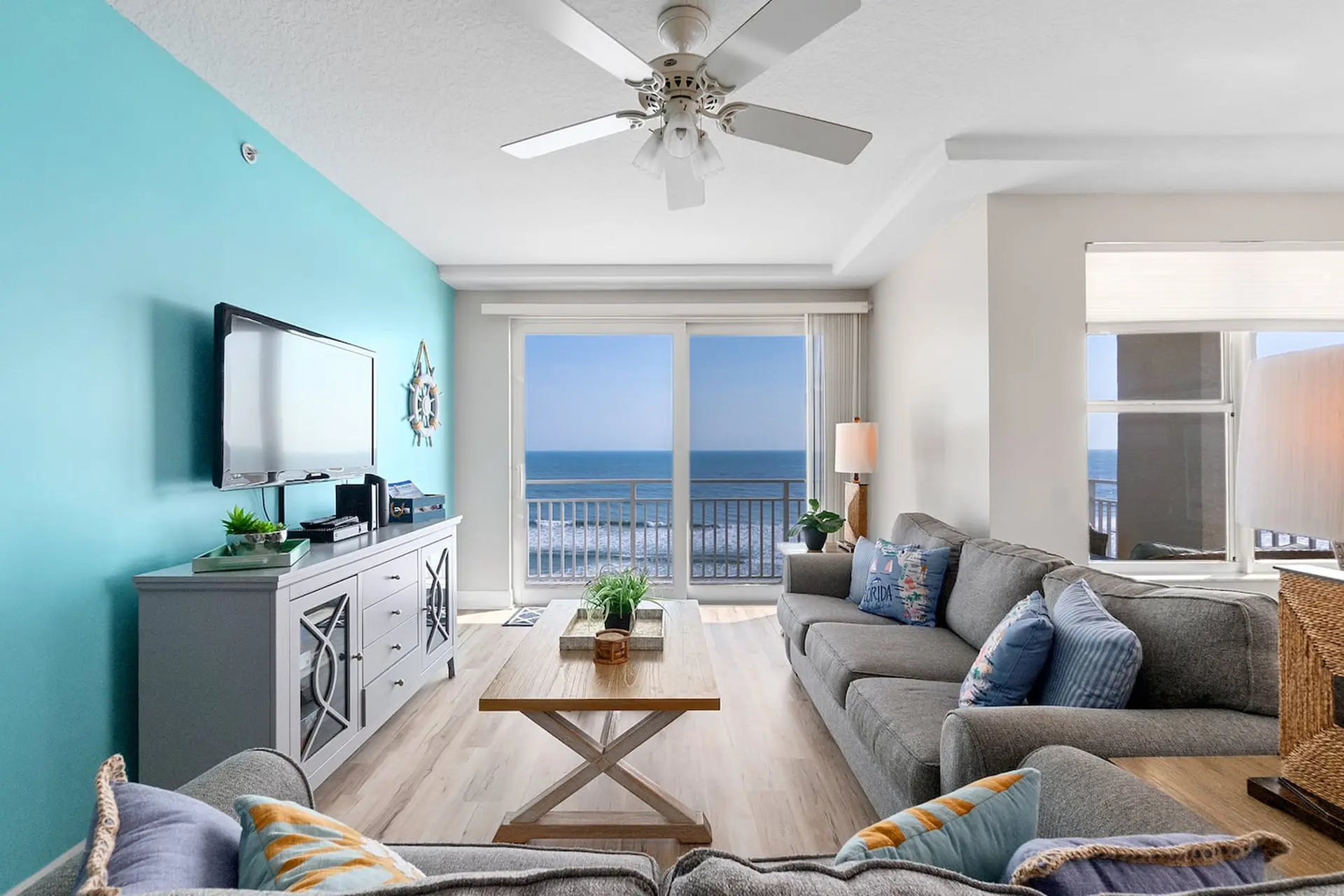 A living room with a sectional sofa, coffee table, and a television facing a balcony with an ocean v