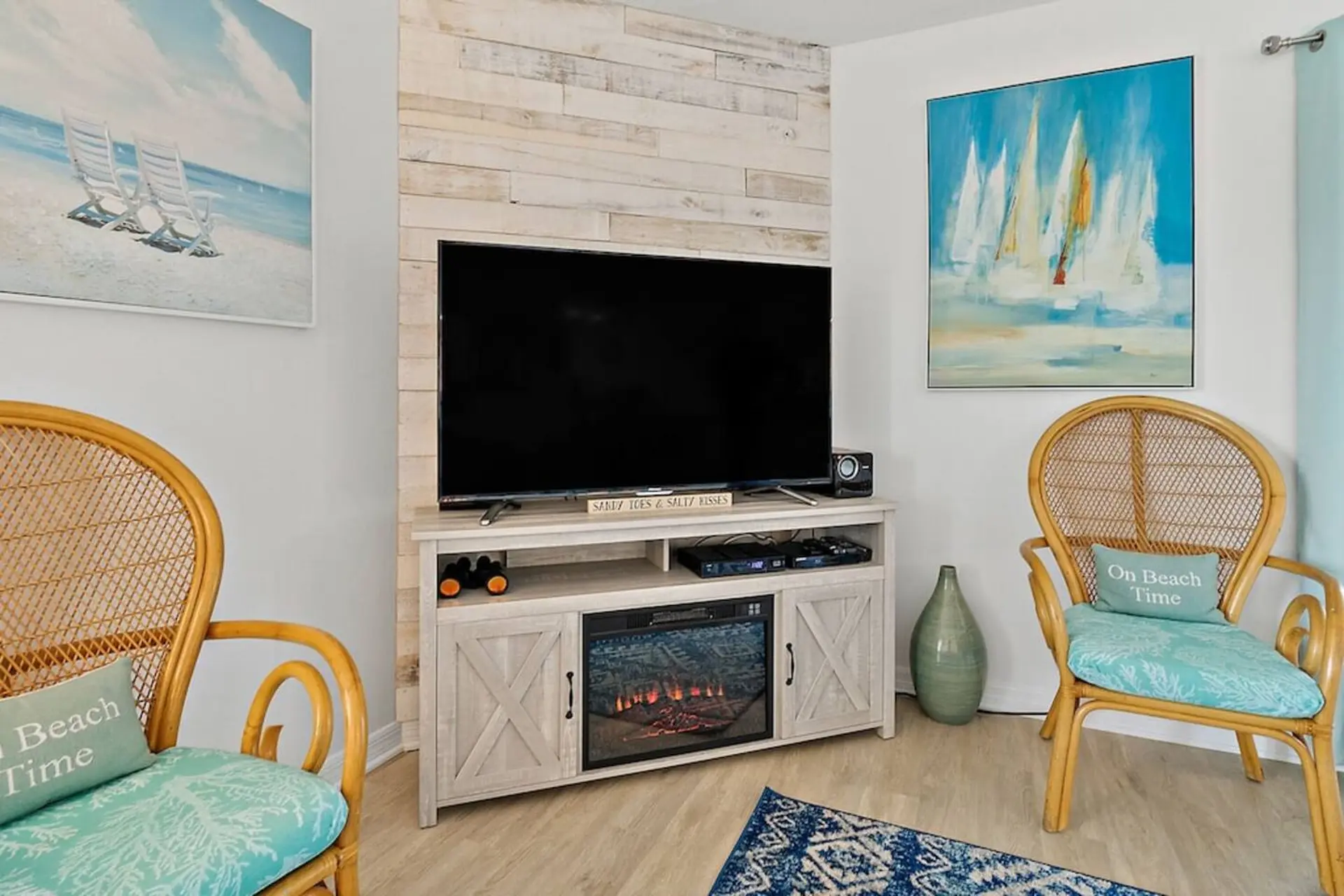 Two wicker chairs with turquoise cushions are placed in front of a fireplace media console.