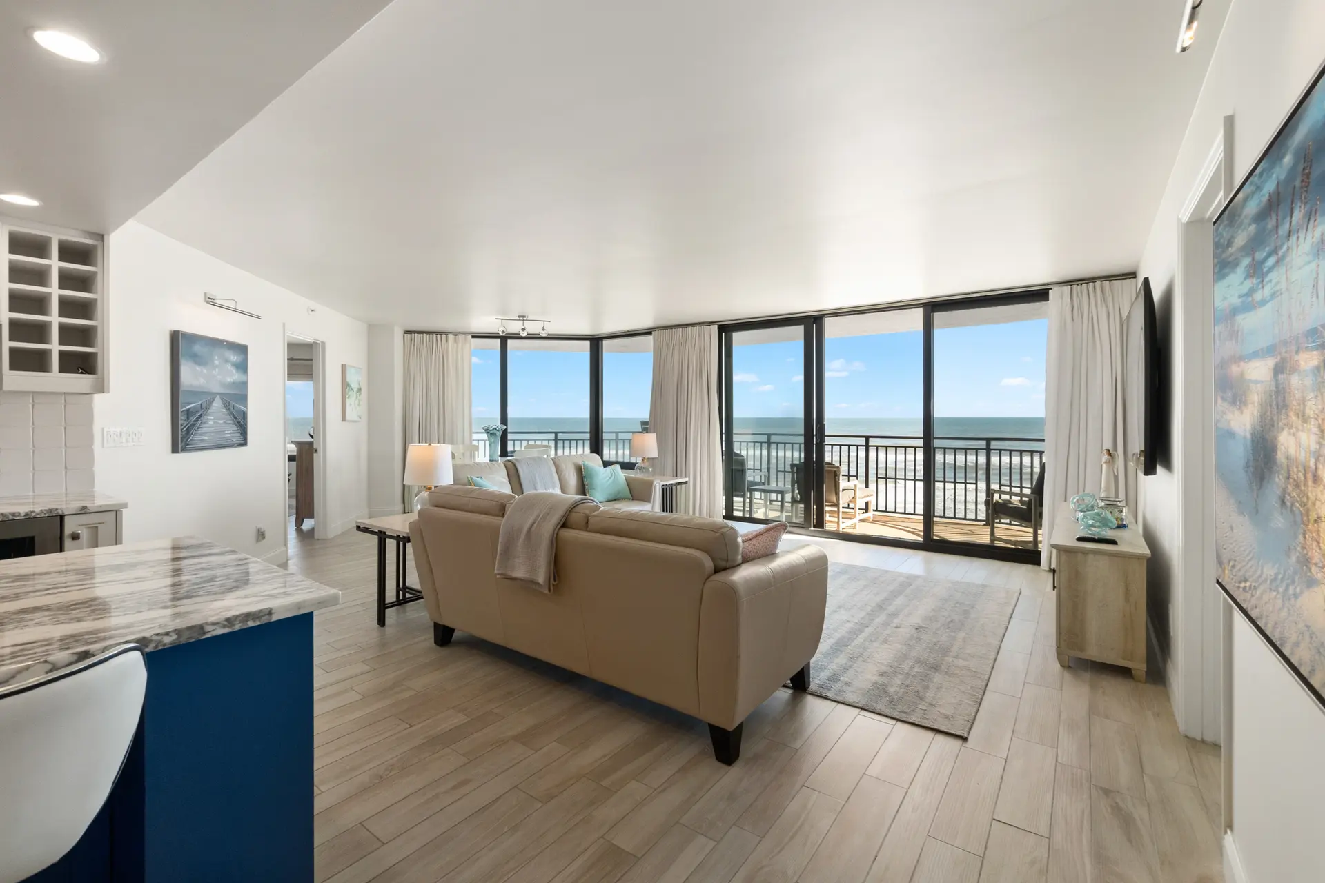 A living room with a beige sofa, wooden floors, and a large window overlooking the ocean.
