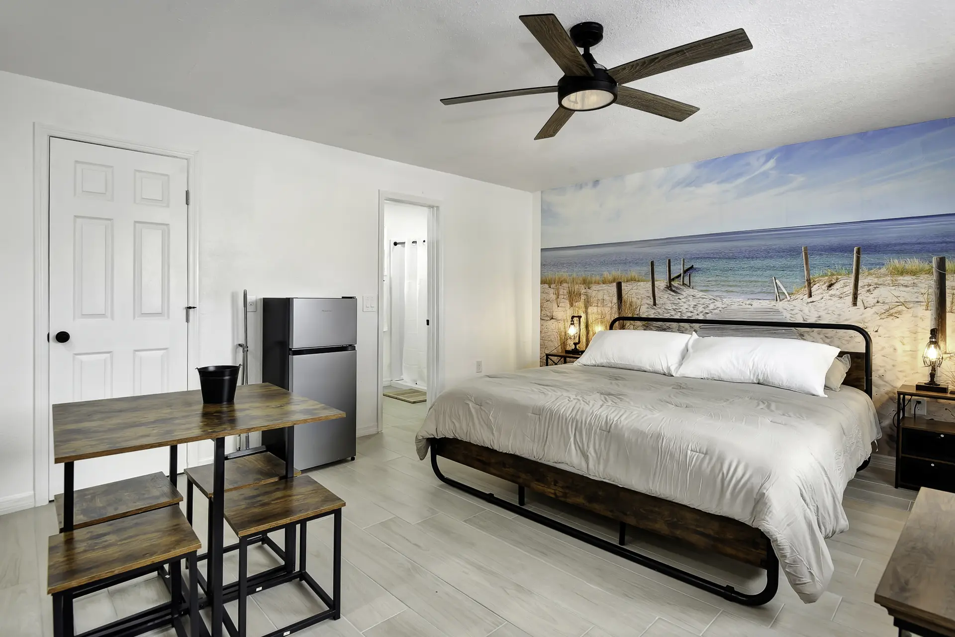 A bedroom with a beach mural, king bed, and a dining table with chairs.