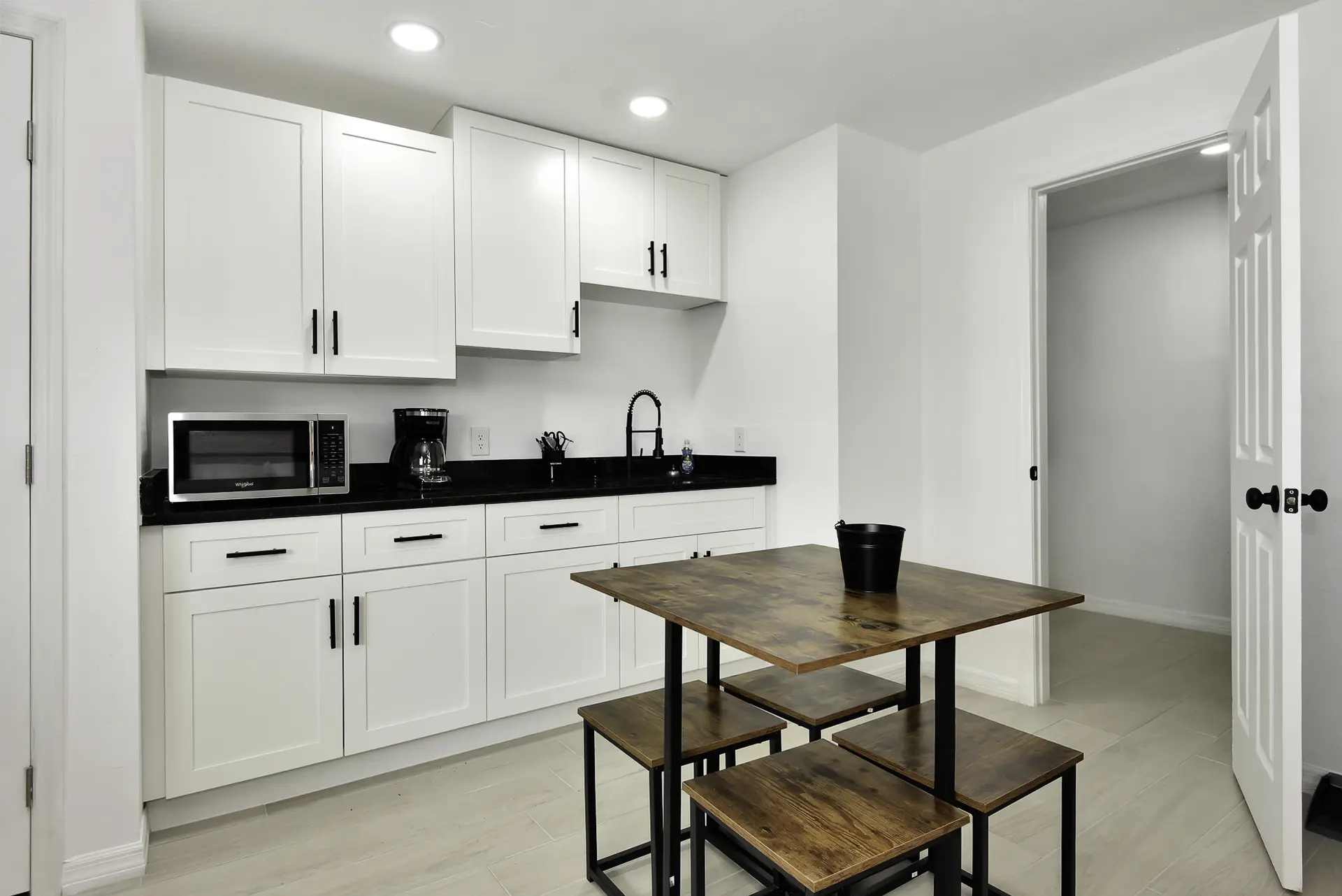 A modern kitchen with white cabinets, black countertops, and a wooden dining set.