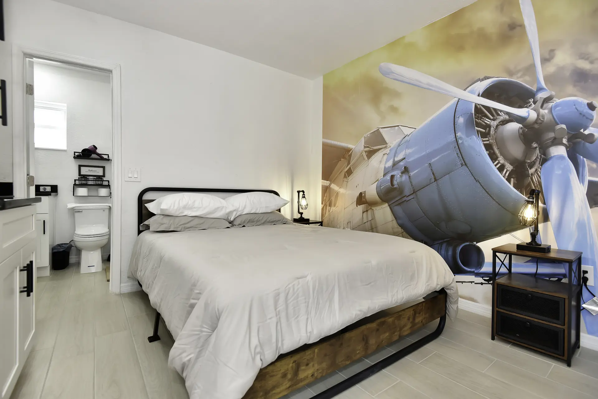 A bedroom with a bed, airplane mural, and adjacent bathroom.