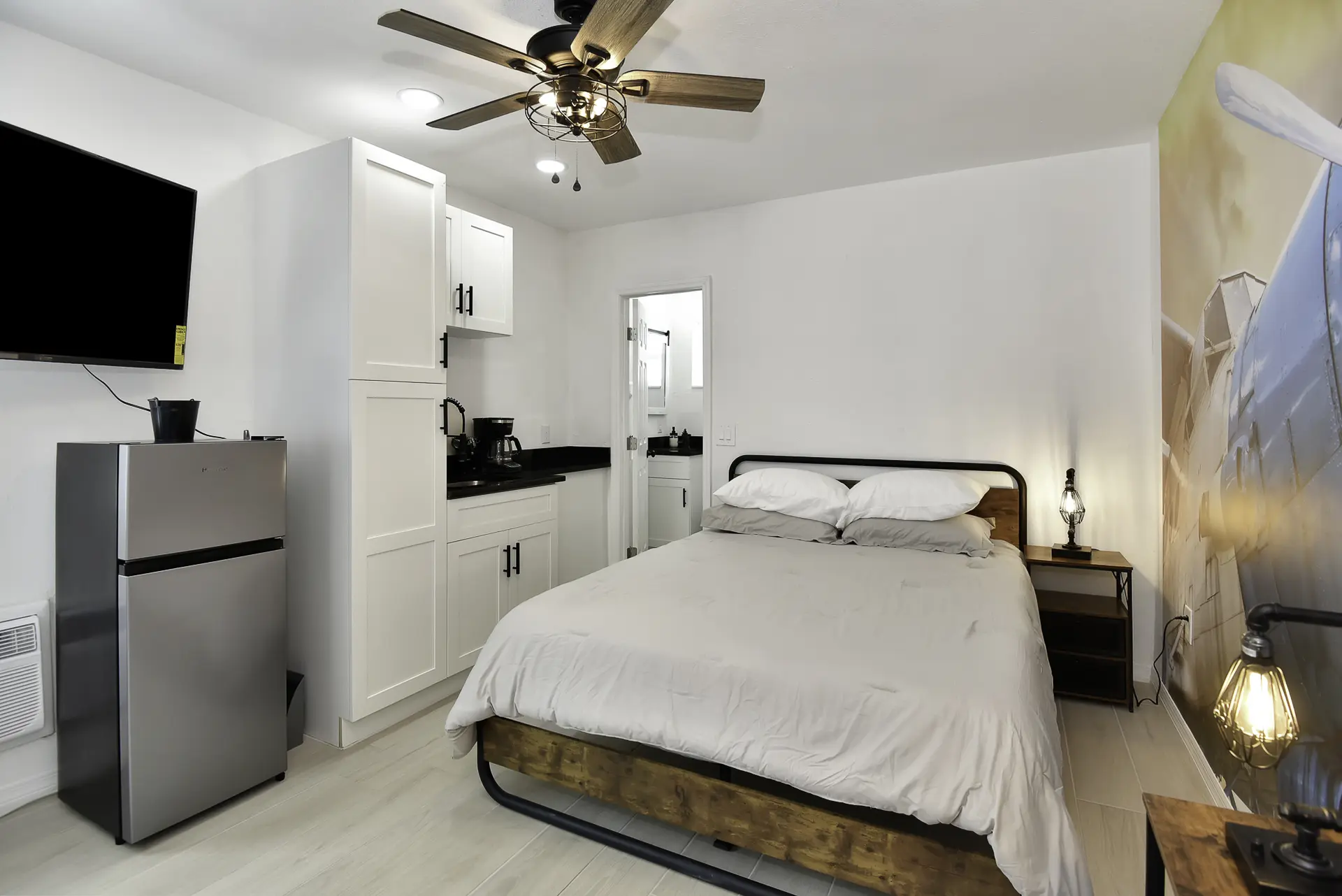 A bedroom with a bed, TV, mini-fridge, and a kitchenette.