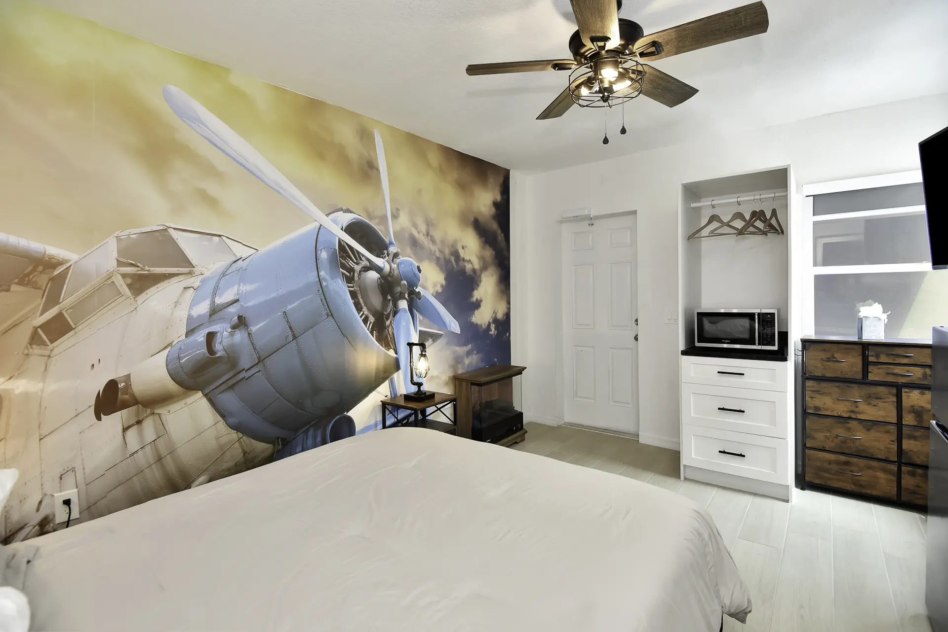 A bedroom with a wall mural of a blue airplane and a white bed.