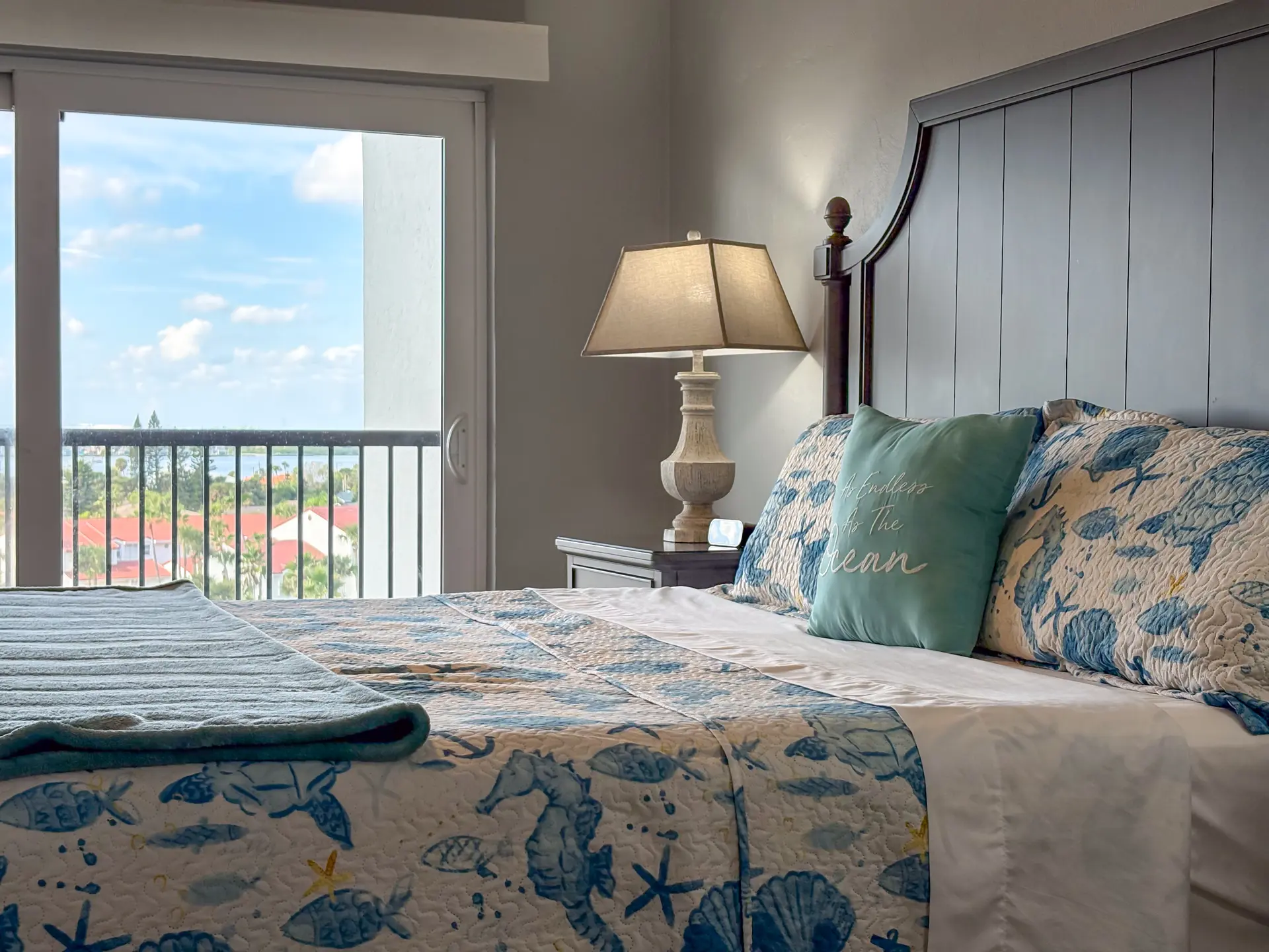 A bed with a marine-themed quilt, two pillows, and a teal pillow with text.