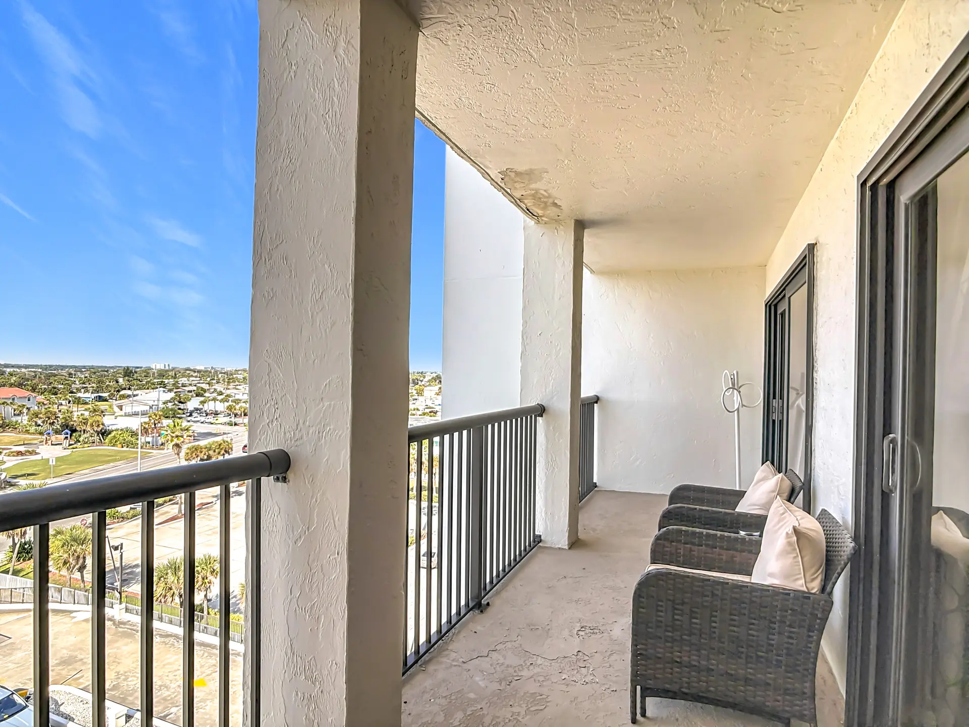 A balcony overlooks a coastal town with palm trees and a clear blue sky.