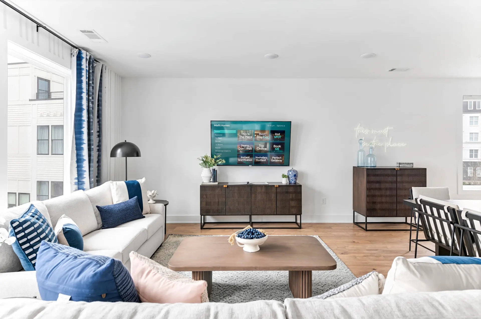 A living room with a large sectional sofa, coffee table, TV, and a neon sign.