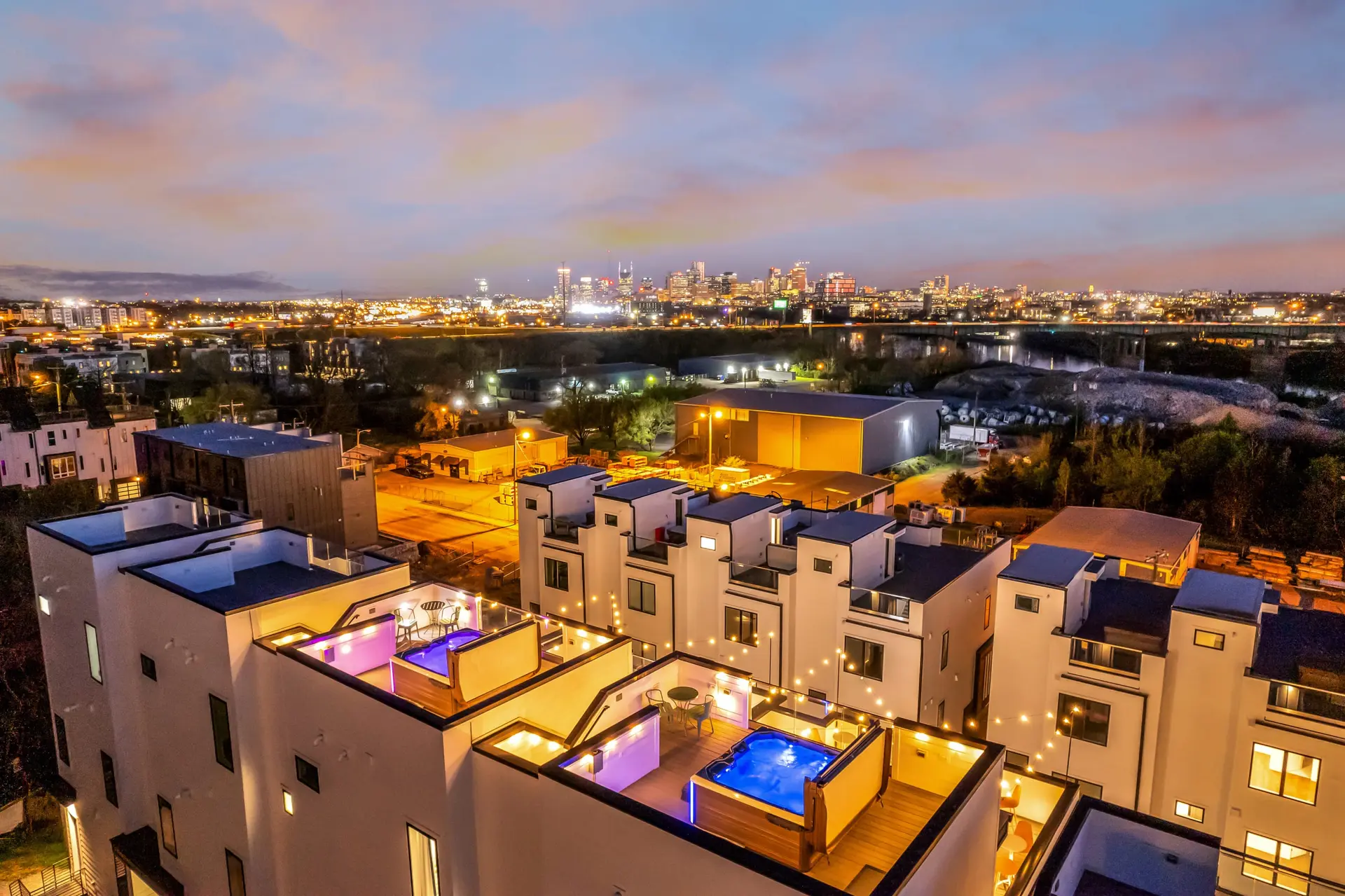A city skyline at dusk with modern white townhomes in the foreground.