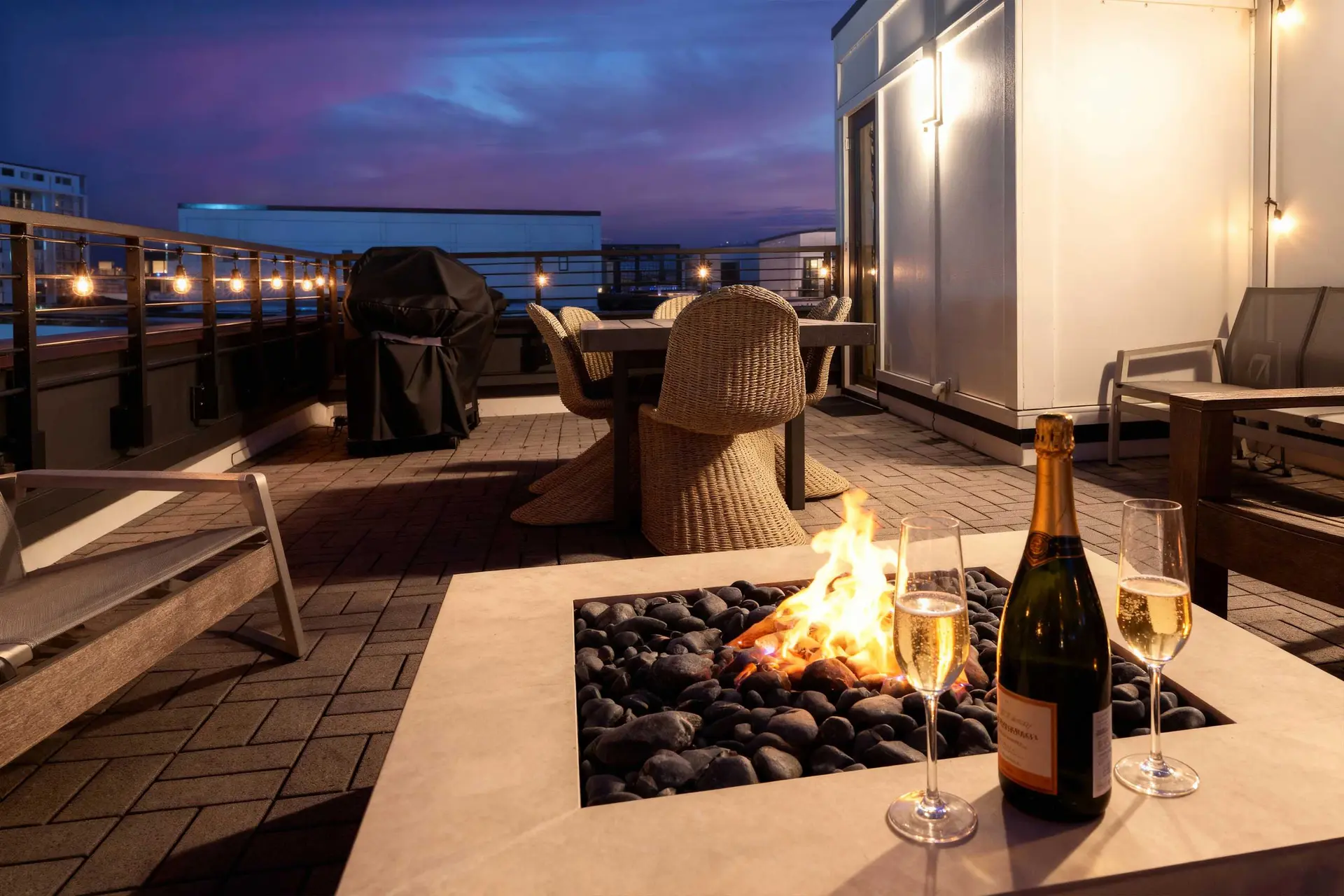 Outdoor patio at dusk with a fire pit, champagne, and chairs.