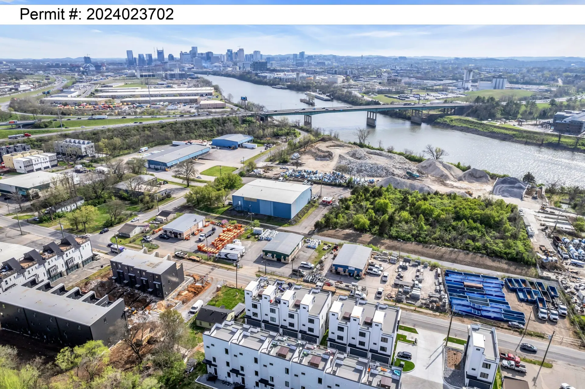 Aerial view of a construction site and cityscape, with a river and bridge in the background.